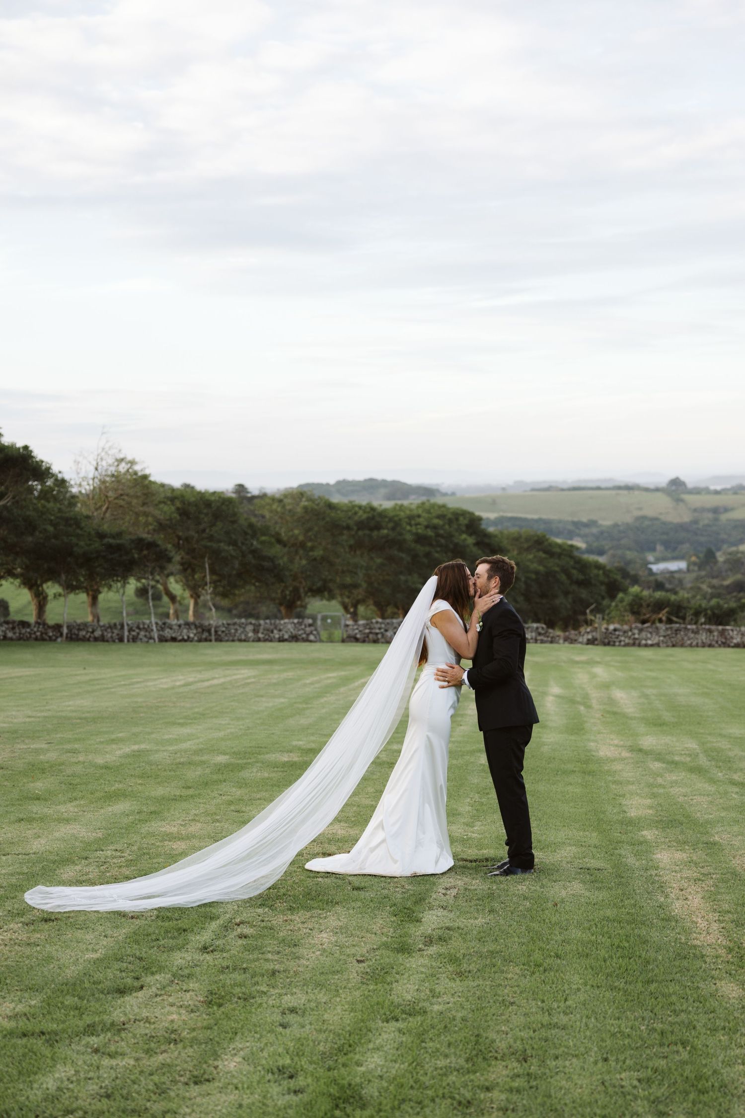 A couple shares an intimate moment during their wedding ceremony on a manicured lawn with rolling hills.