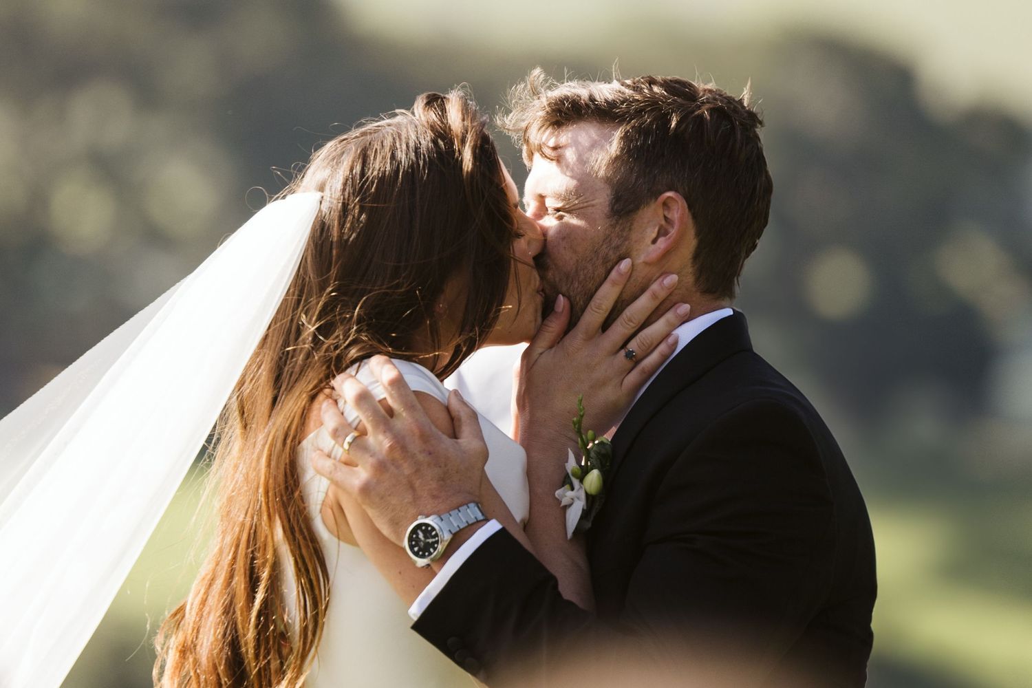 Intimate wedding kiss captured against a backdrop of rolling hills and natural landscape.