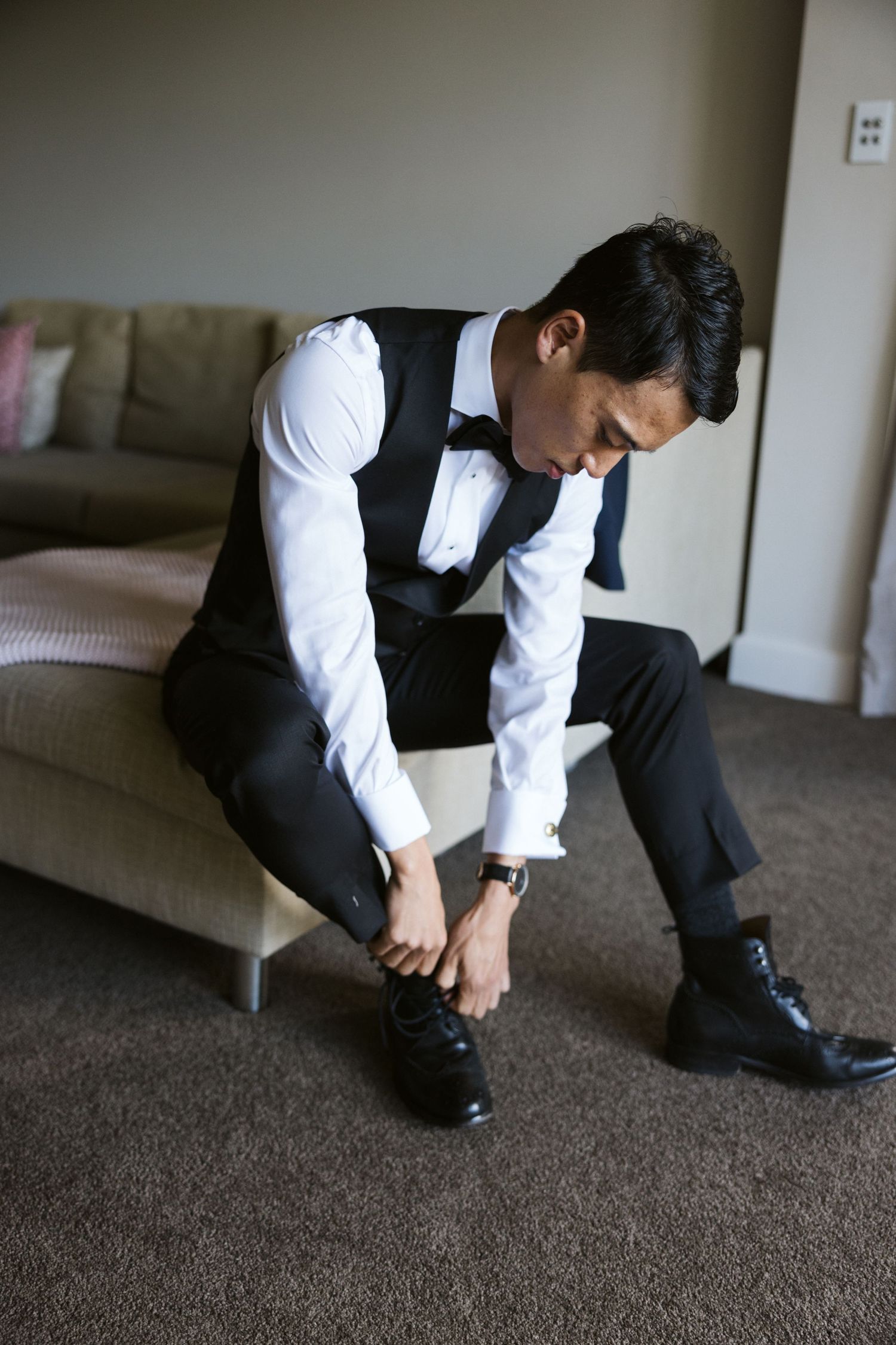 Person in formal attire sitting on couch while putting on dress shoes.