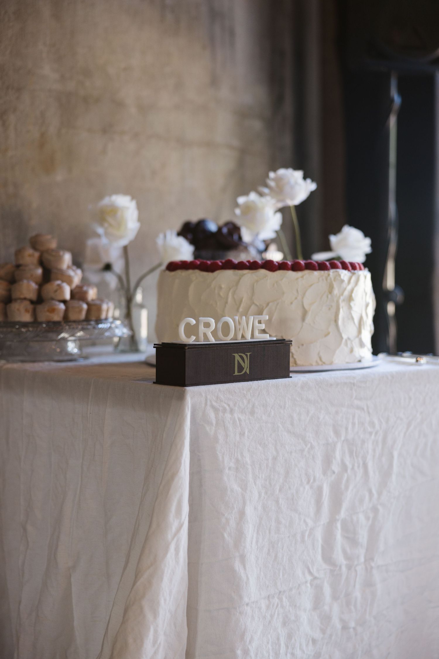 Elegant white wedding cake decorated with fresh flowers and personalized name display.
