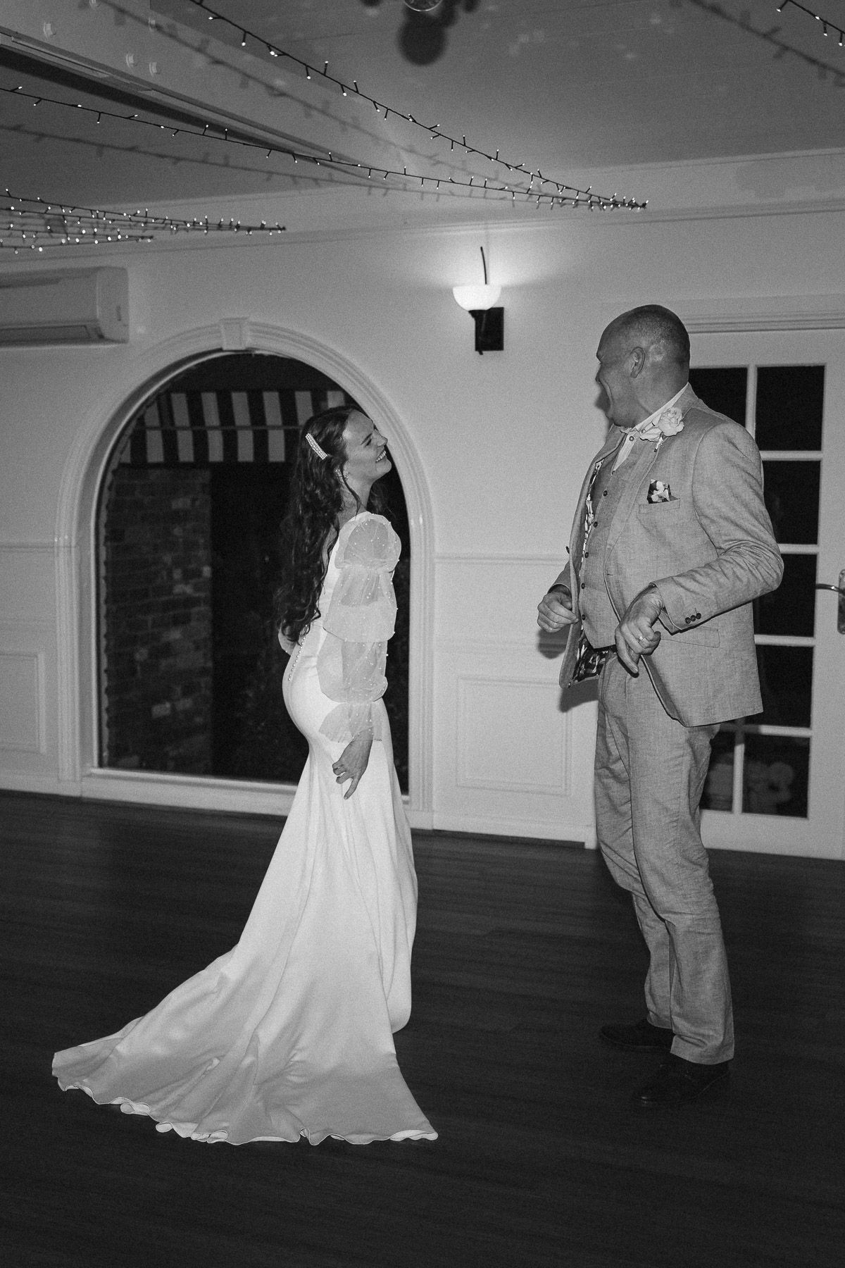 Bride and groom sharing first dance in elegant venue with fairy lights in black and white.