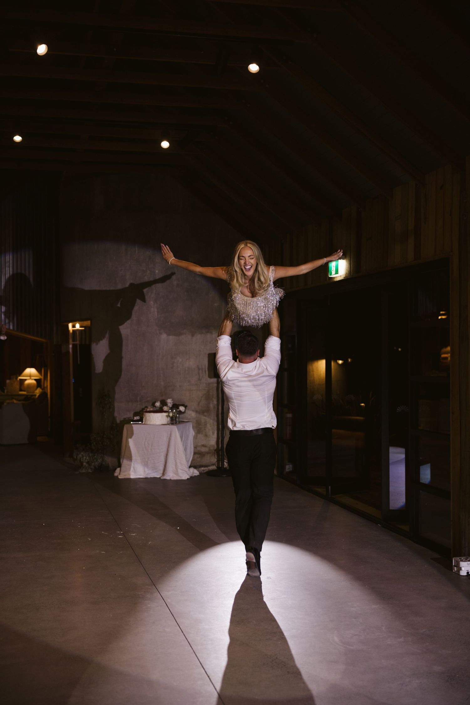 A dramatic spotlight illuminates a wedding couple performing a lift dance move in a dark venue.