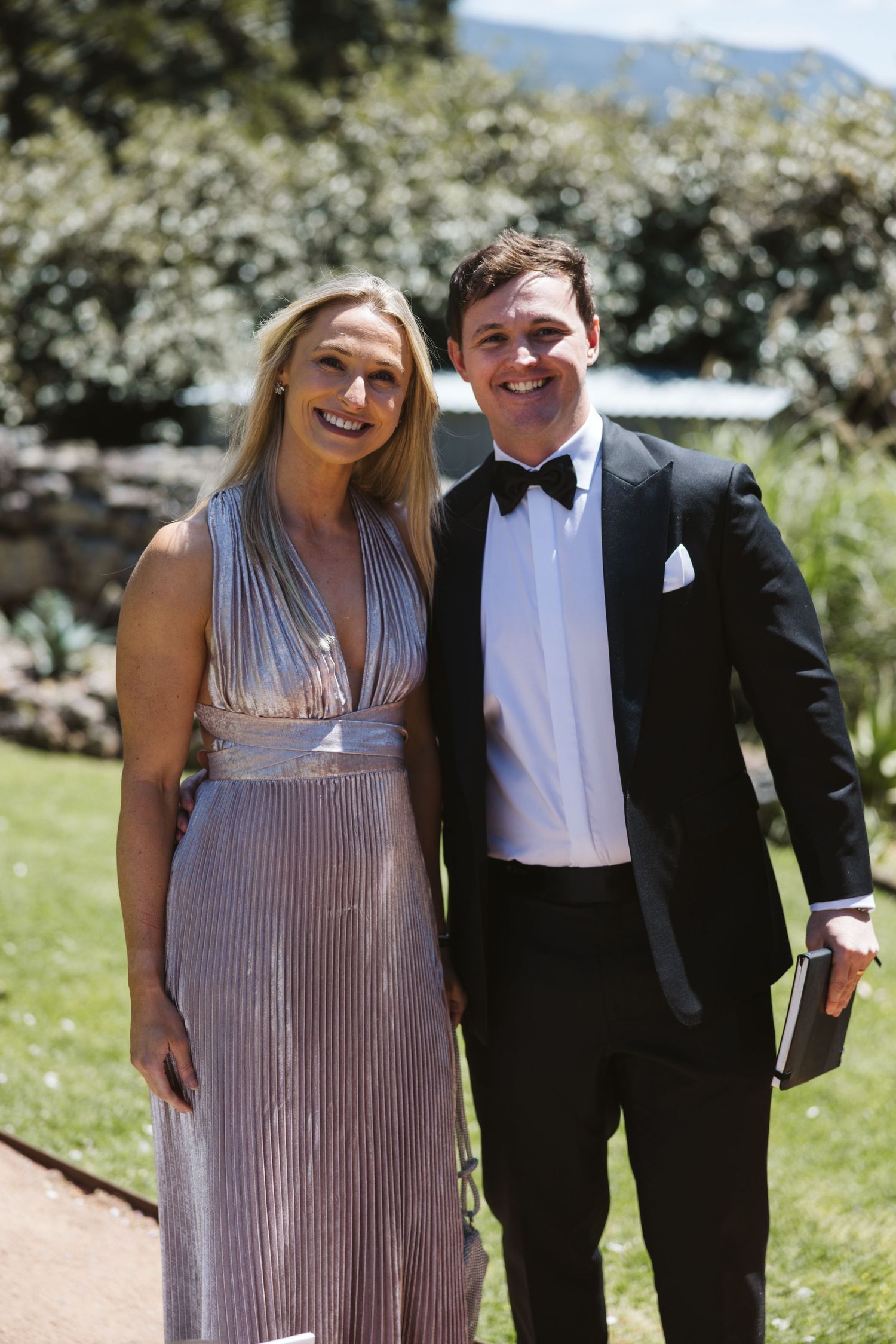 Couple in formal attire poses on garden path during outdoor event.
