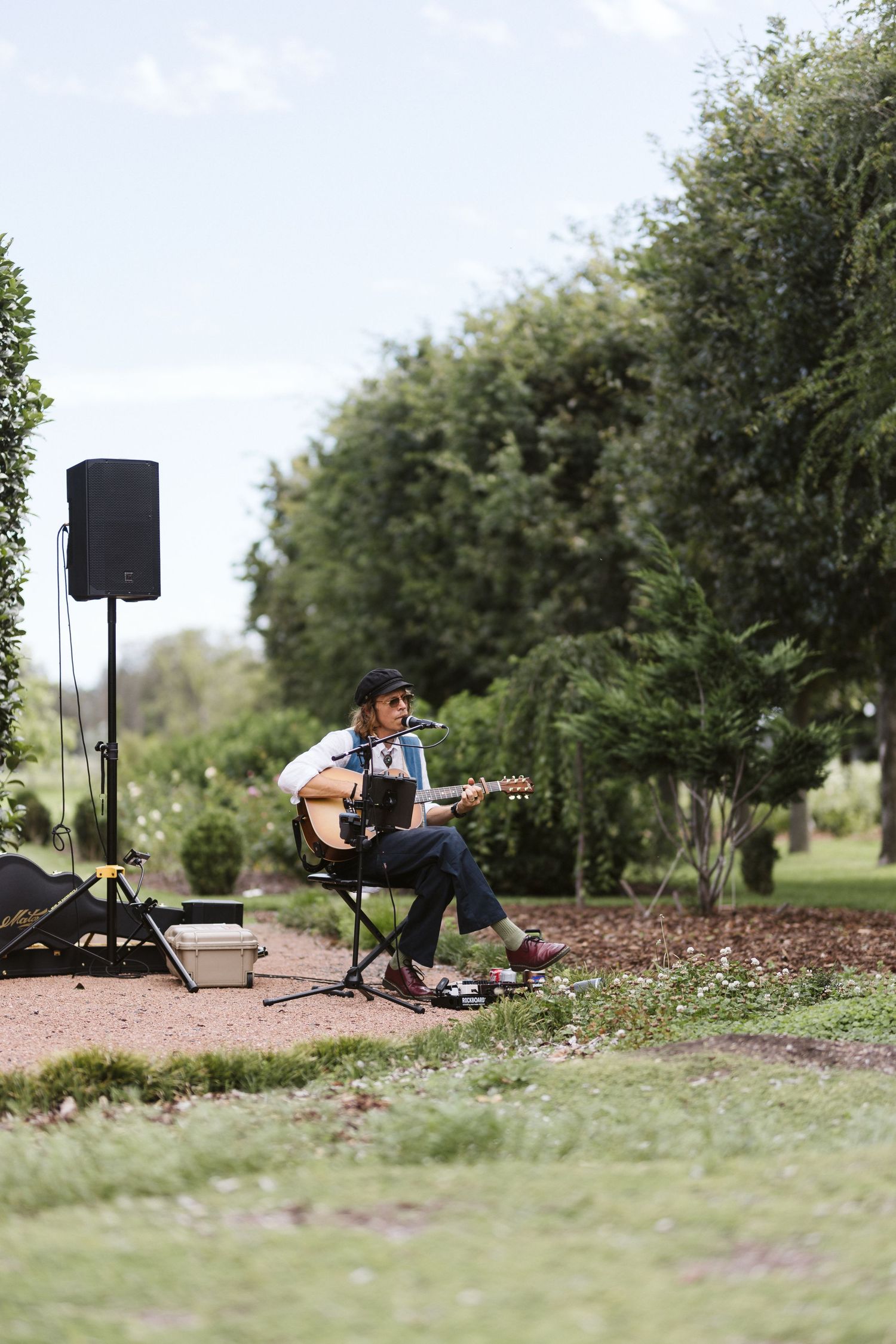 Outdoor musician performing with acoustic guitar near landscaped garden path.