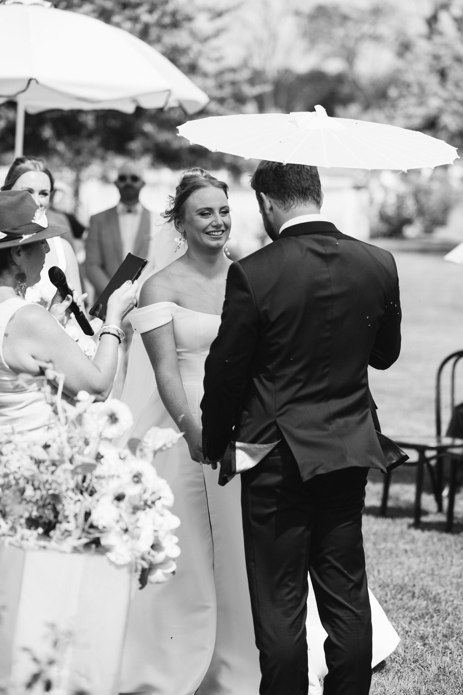 Black and white photo of wedding celebration with parasols in an outdoor garden setting.
