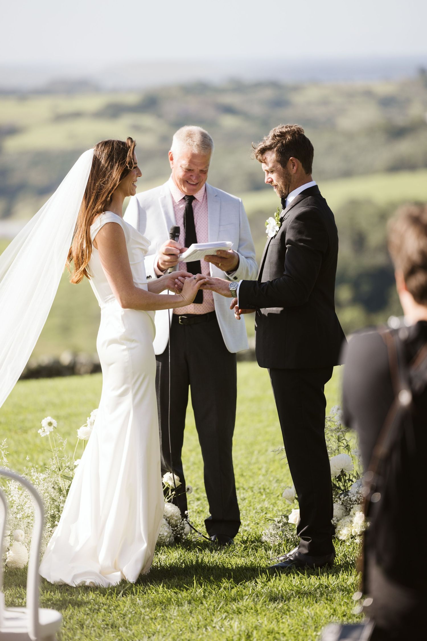 Outdoor wedding ceremony with rolling hills in the background as couple exchanges rings.
