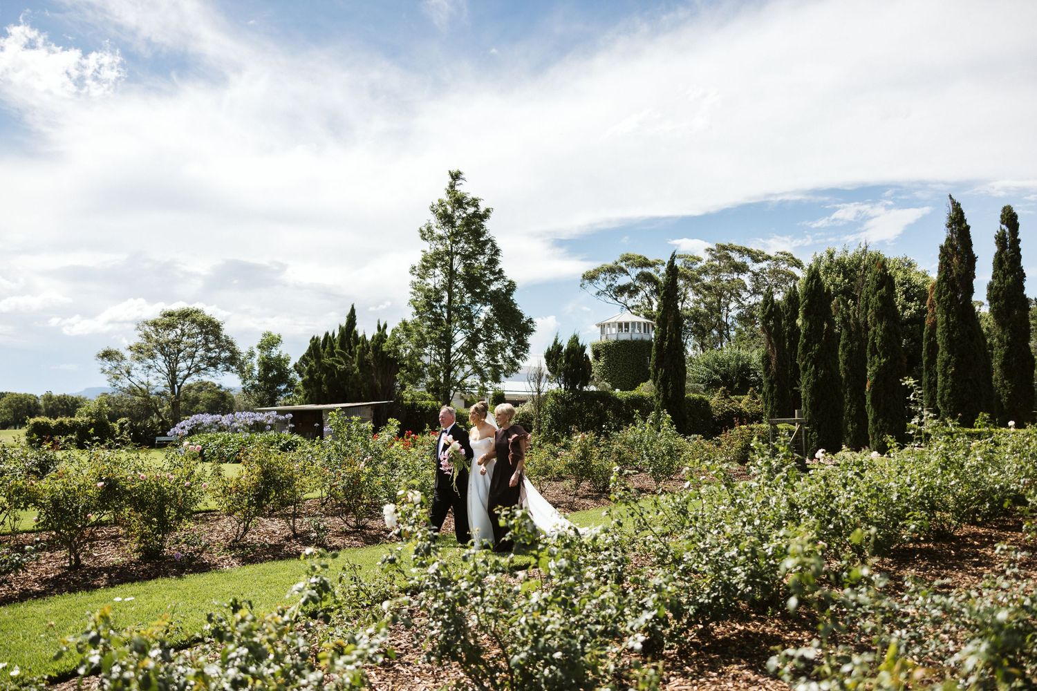 A wedding ceremony in a lush garden landscape with cypress trees and blue skies.