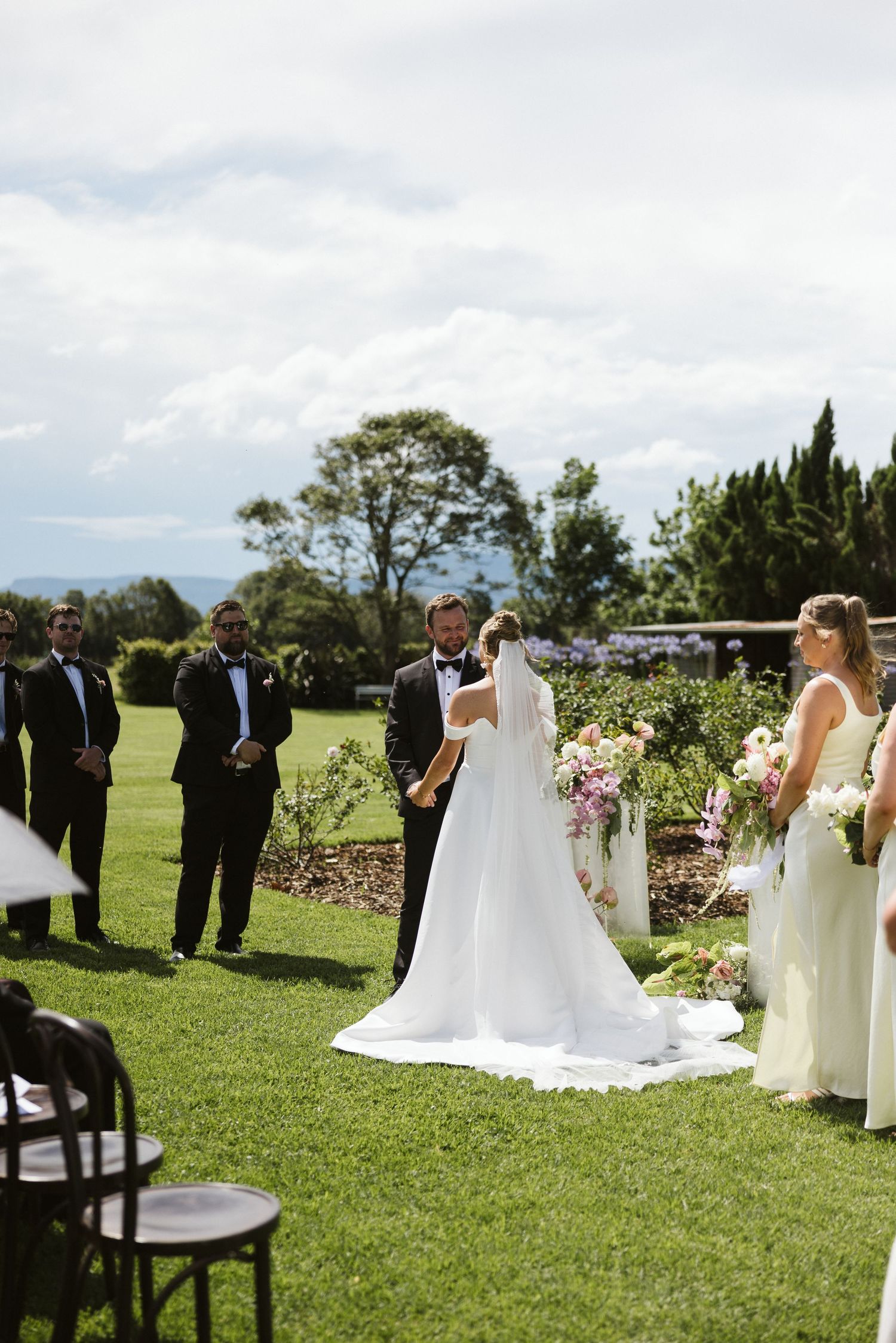 An outdoor wedding ceremony in a manicured garden with white chairs and floral arrangements.