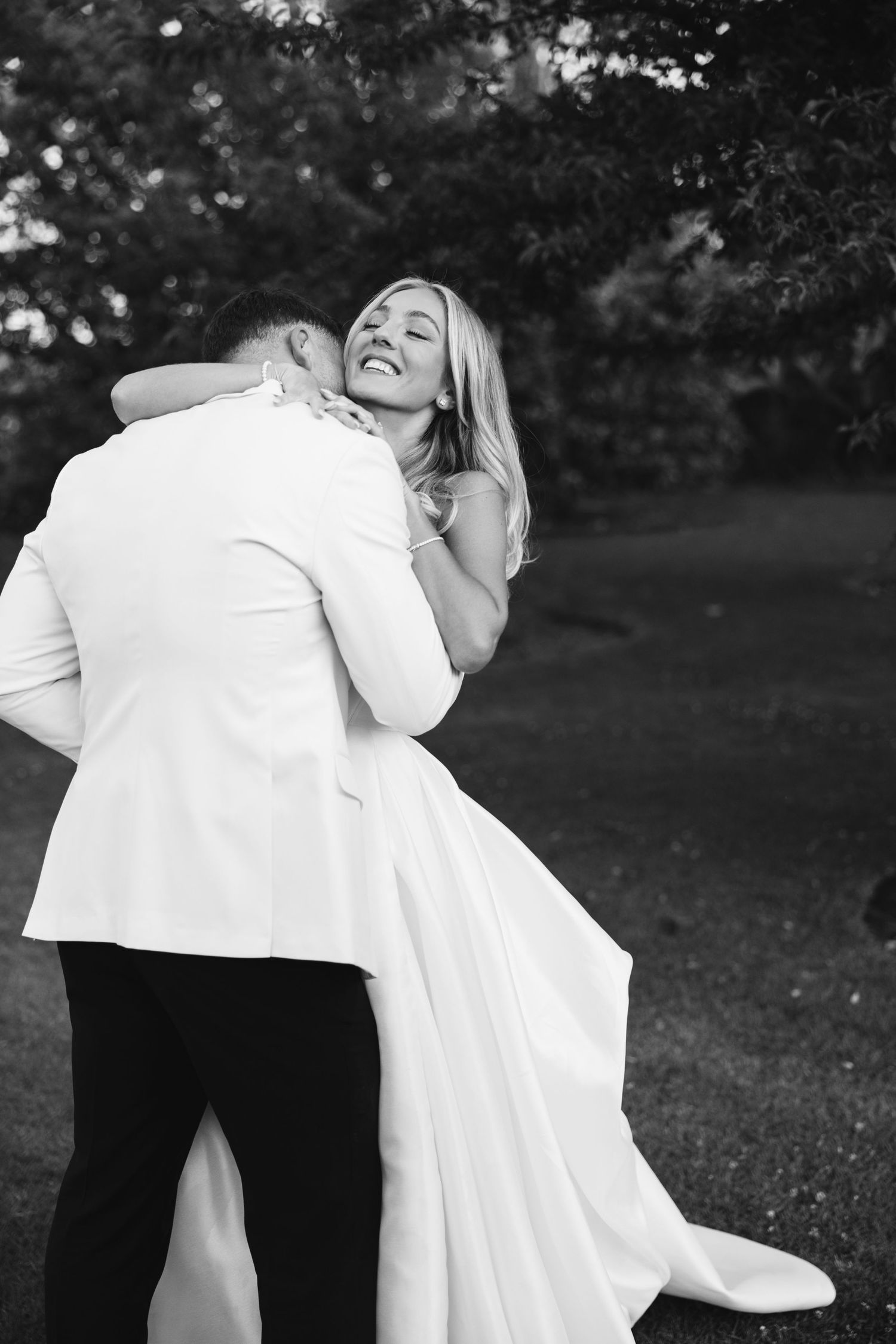 Black and white candid of newlyweds sharing a joyful embrace outdoors.