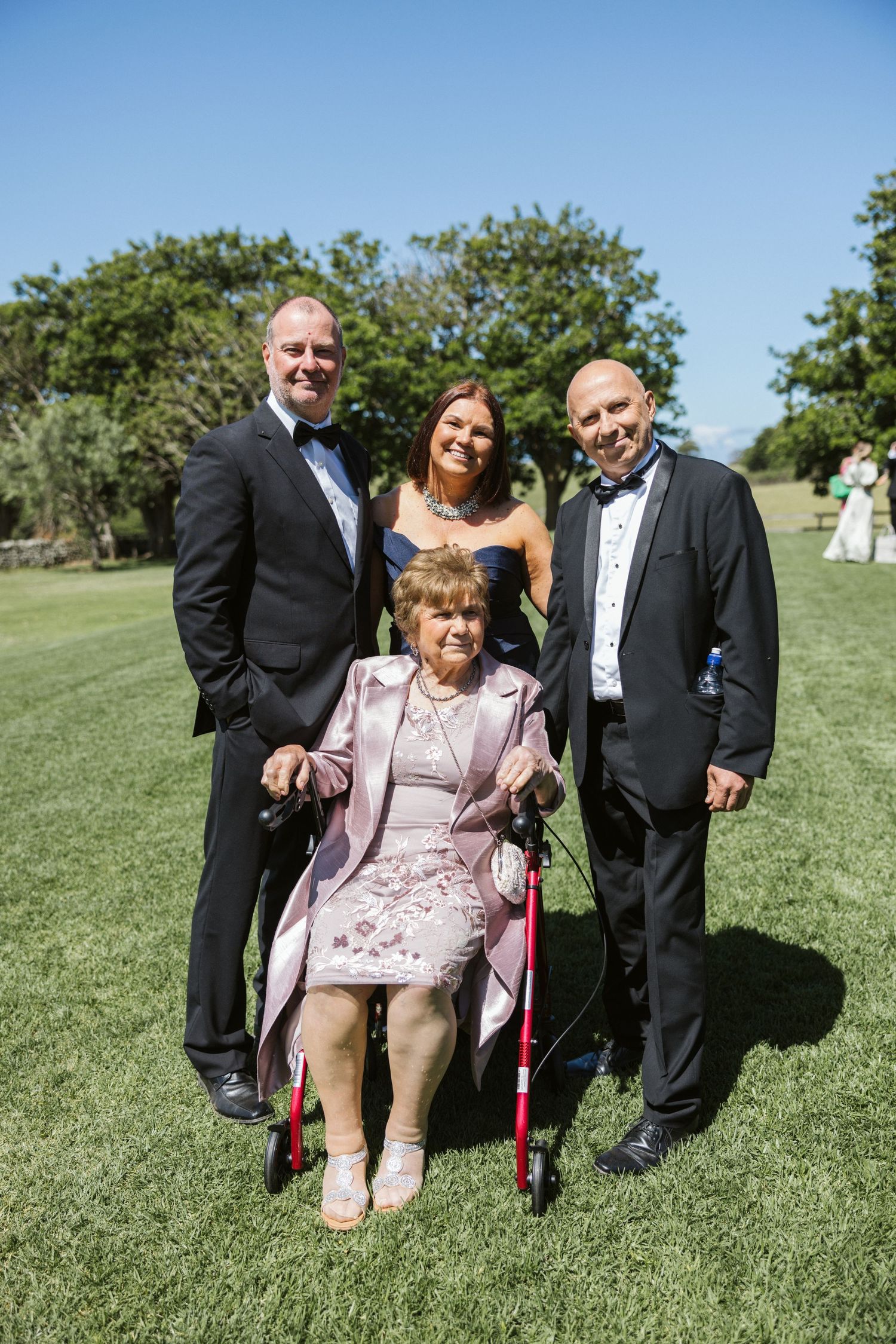Formal gathering at an outdoor event with four people posing together on a sunny lawn.