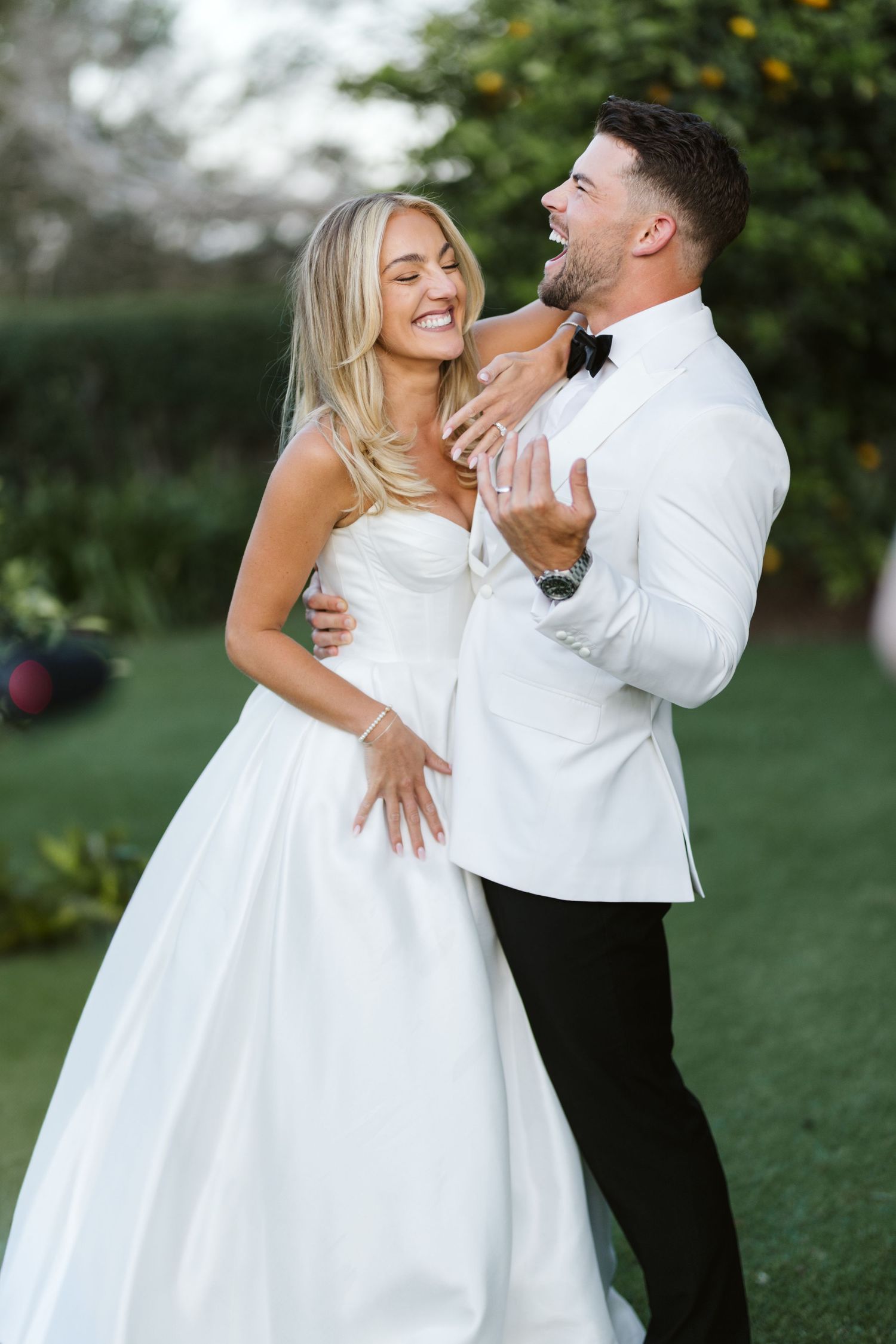 Happy couple in wedding attire sharing a lighthearted moment while embracing outdoors.