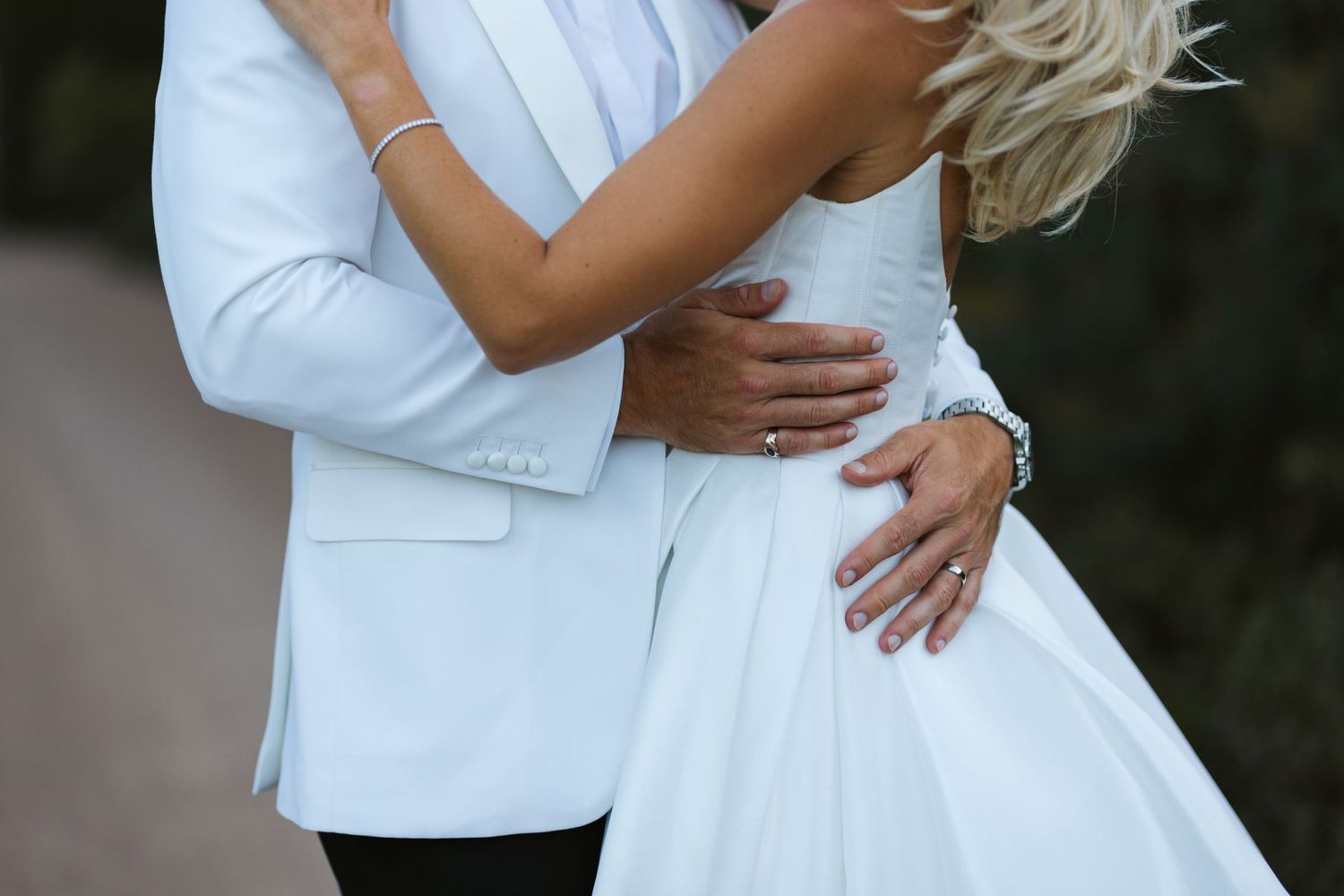 Close-up of newlyweds embracing, showing white wedding dress and suit details.