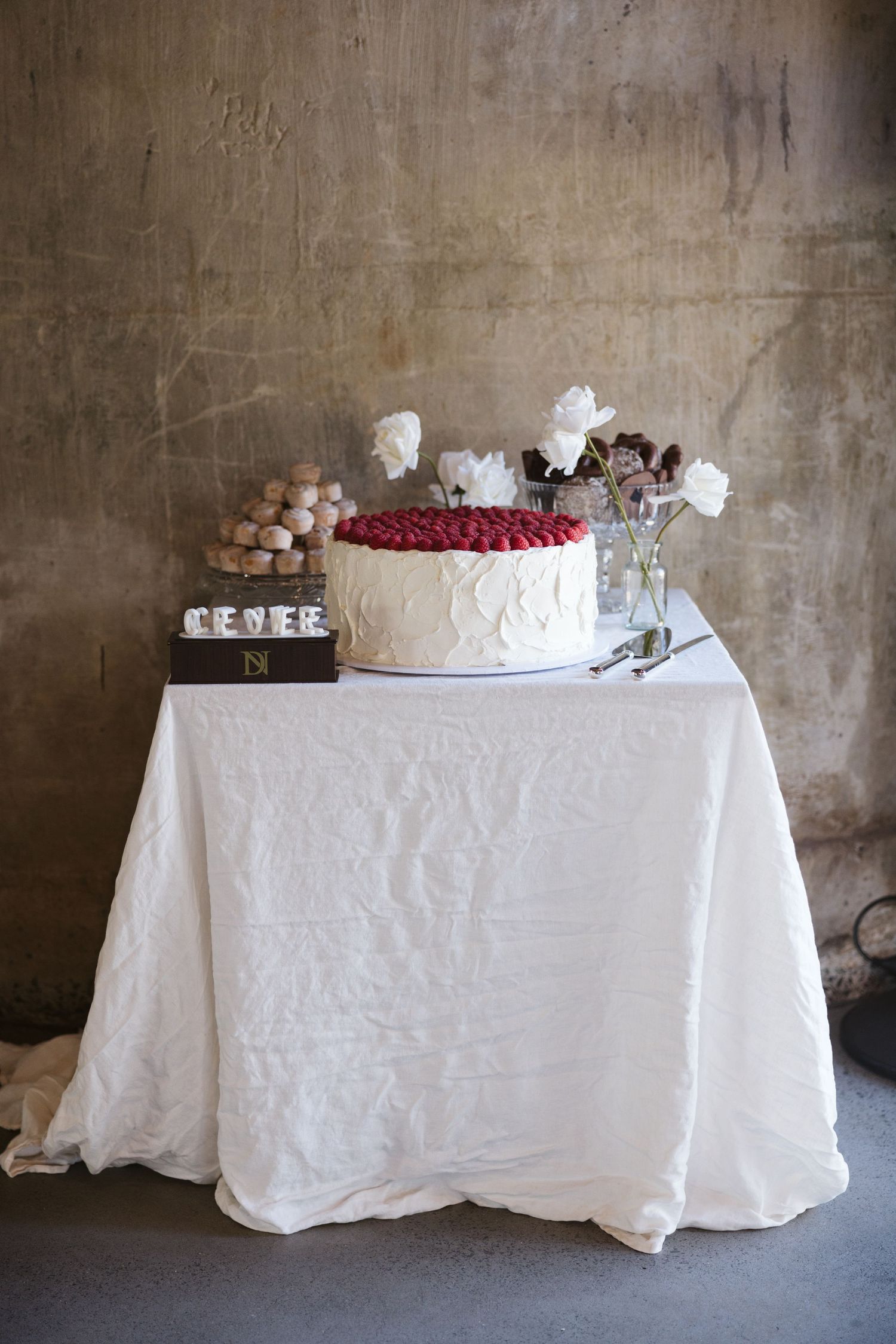 White wedding cake with red berry accents and floral decorations on crisp white tablecloth.