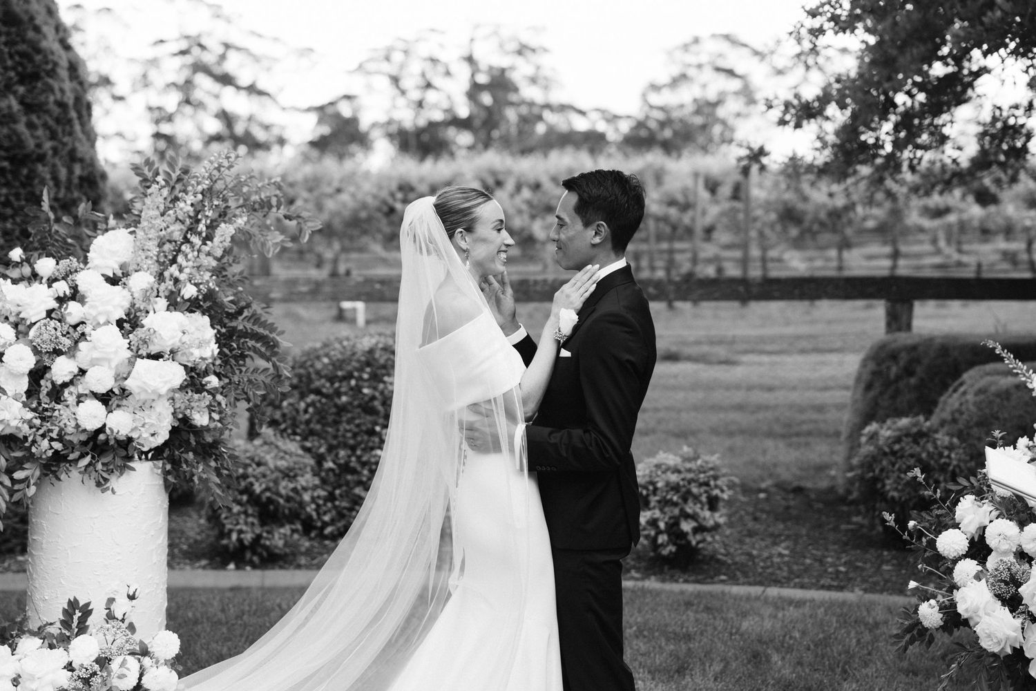 Wedding ceremony moment in garden with white floral arrangements.
