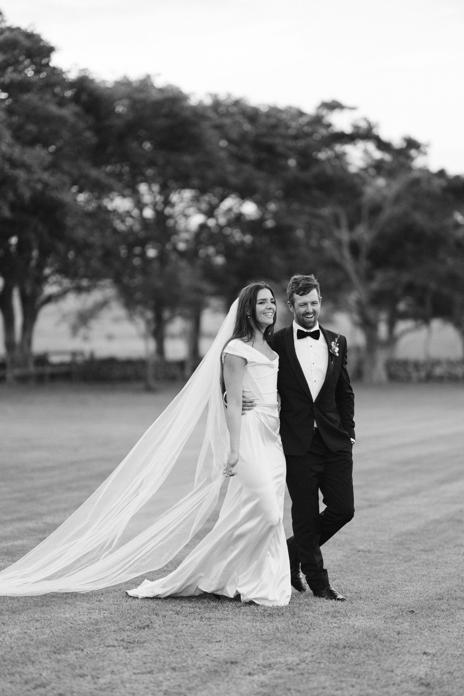 Elegant black and white portrait of a couple in wedding attire standing on manicured grounds.