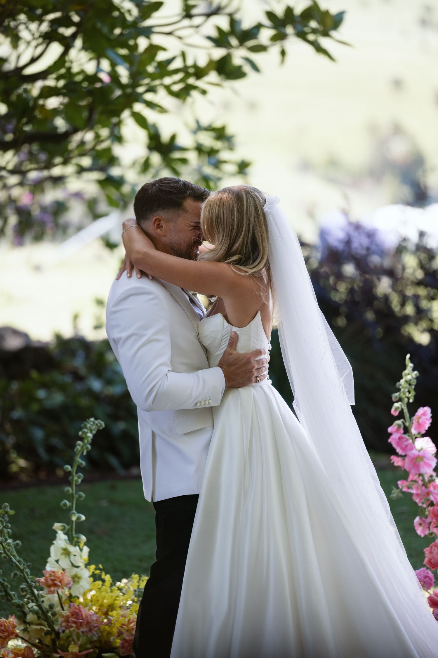 Intimate embrace during wedding ceremony surrounded by colorful garden flowers.
