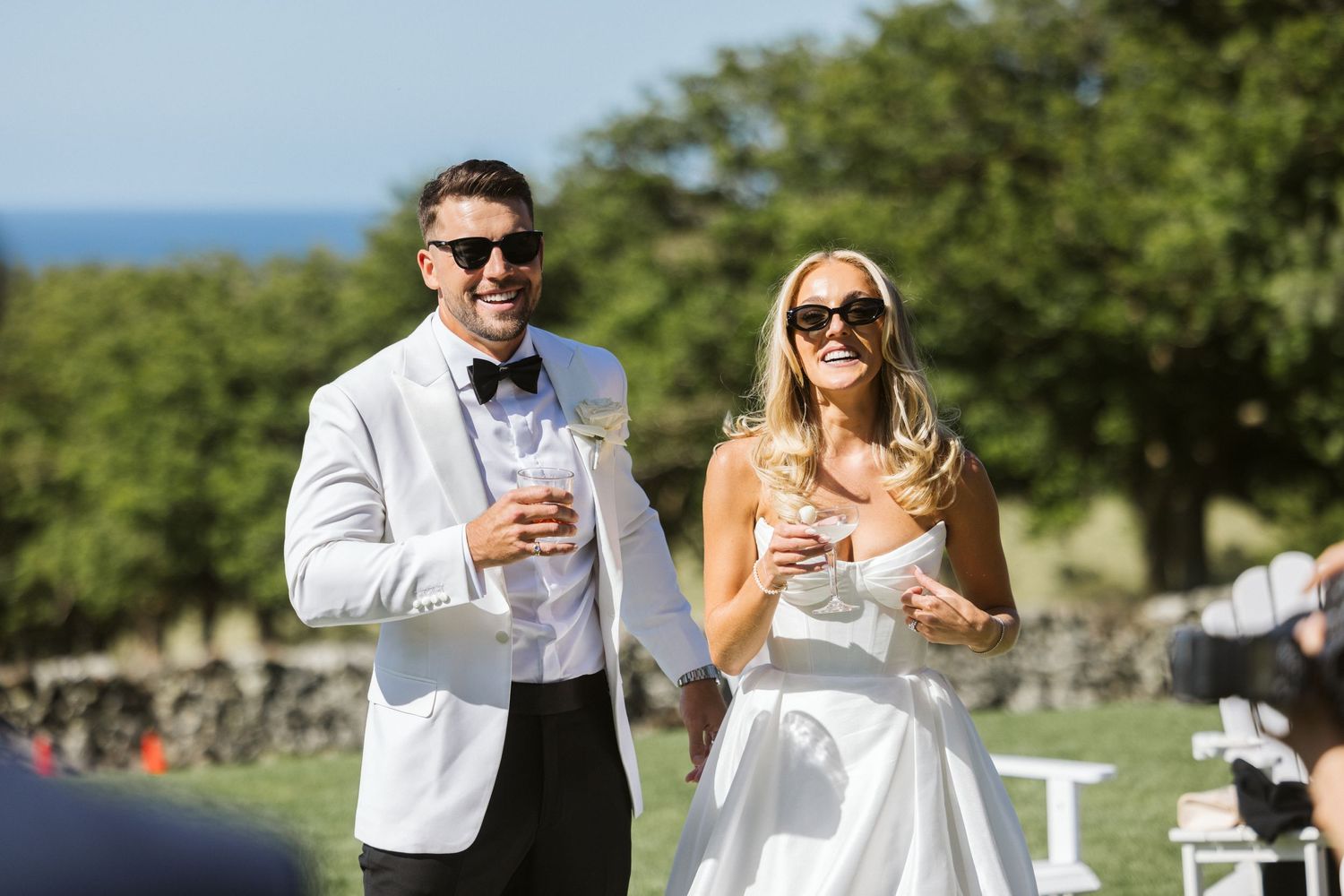 Newlyweds sharing drinks outdoors at an elegant wedding celebration with scenic views.