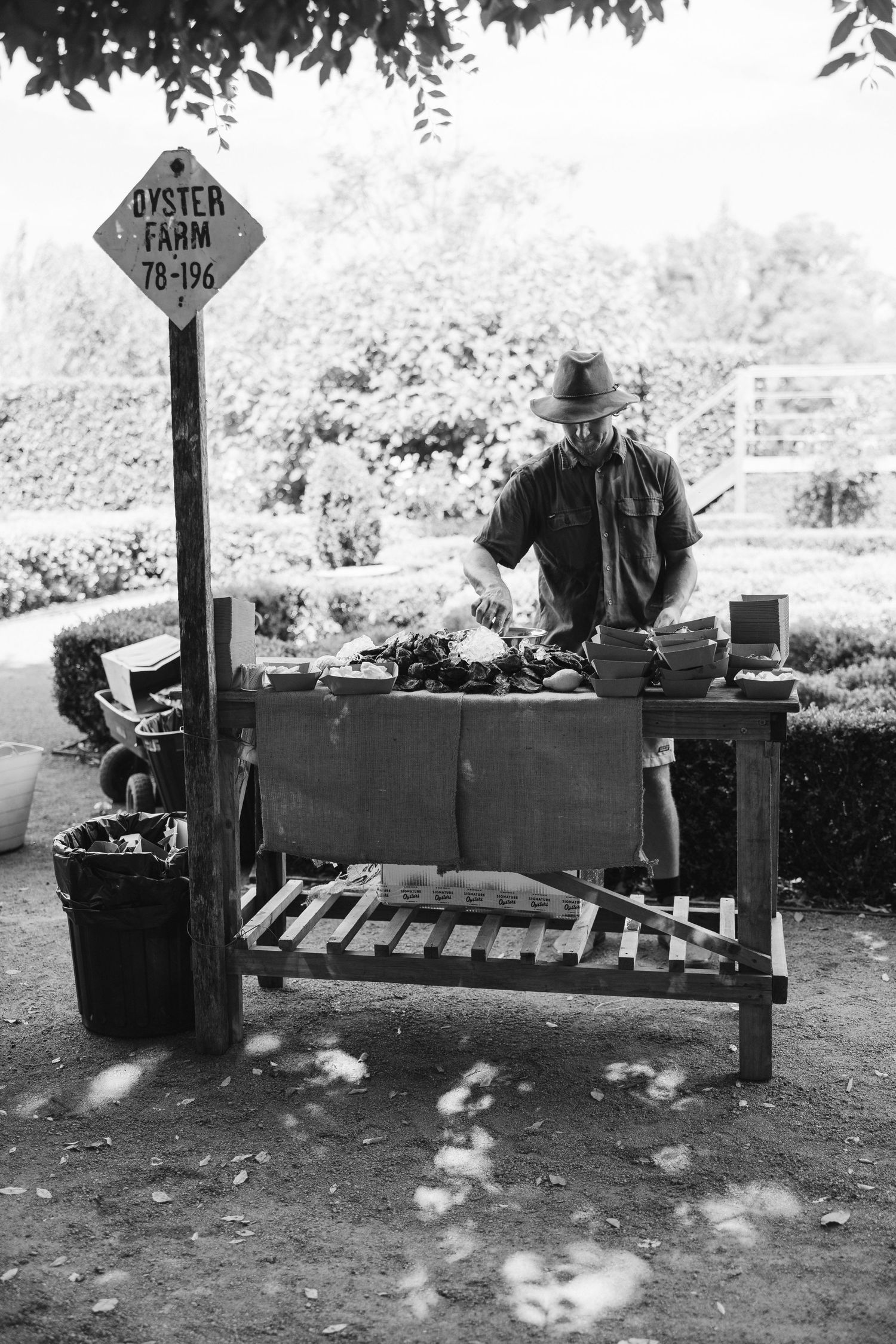 Black and white image of oyster station with vendor preparing fresh seafood outdoors.