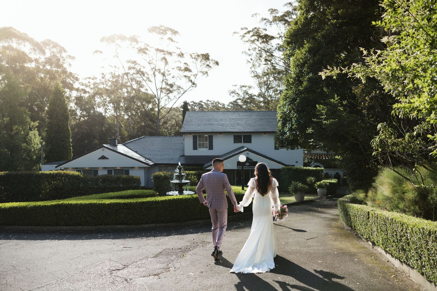 A couple walks down a tree-lined rural road during sunset, creating a romantic silhouette against the golden sky.