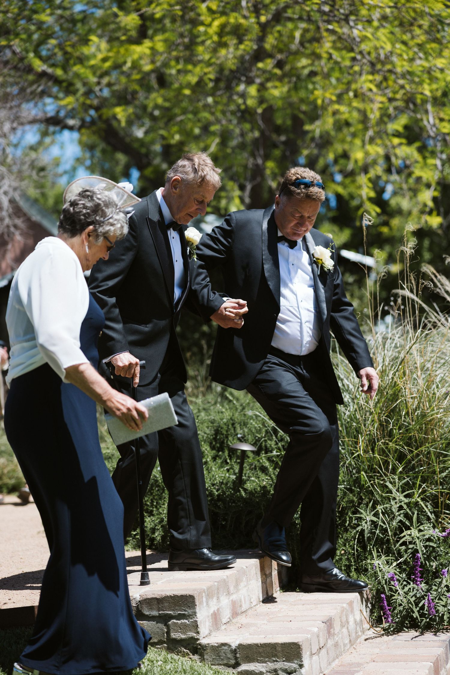 Wedding guests carefully navigate stone steps in an outdoor garden setting.
