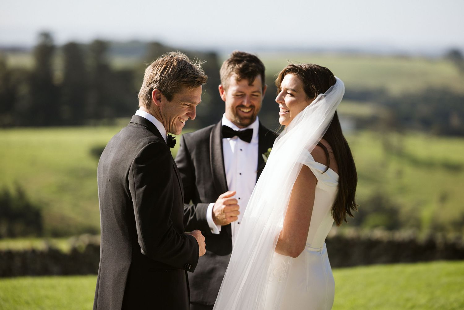 Wedding ceremony moment with couple and officiant sharing a laugh outdoors.