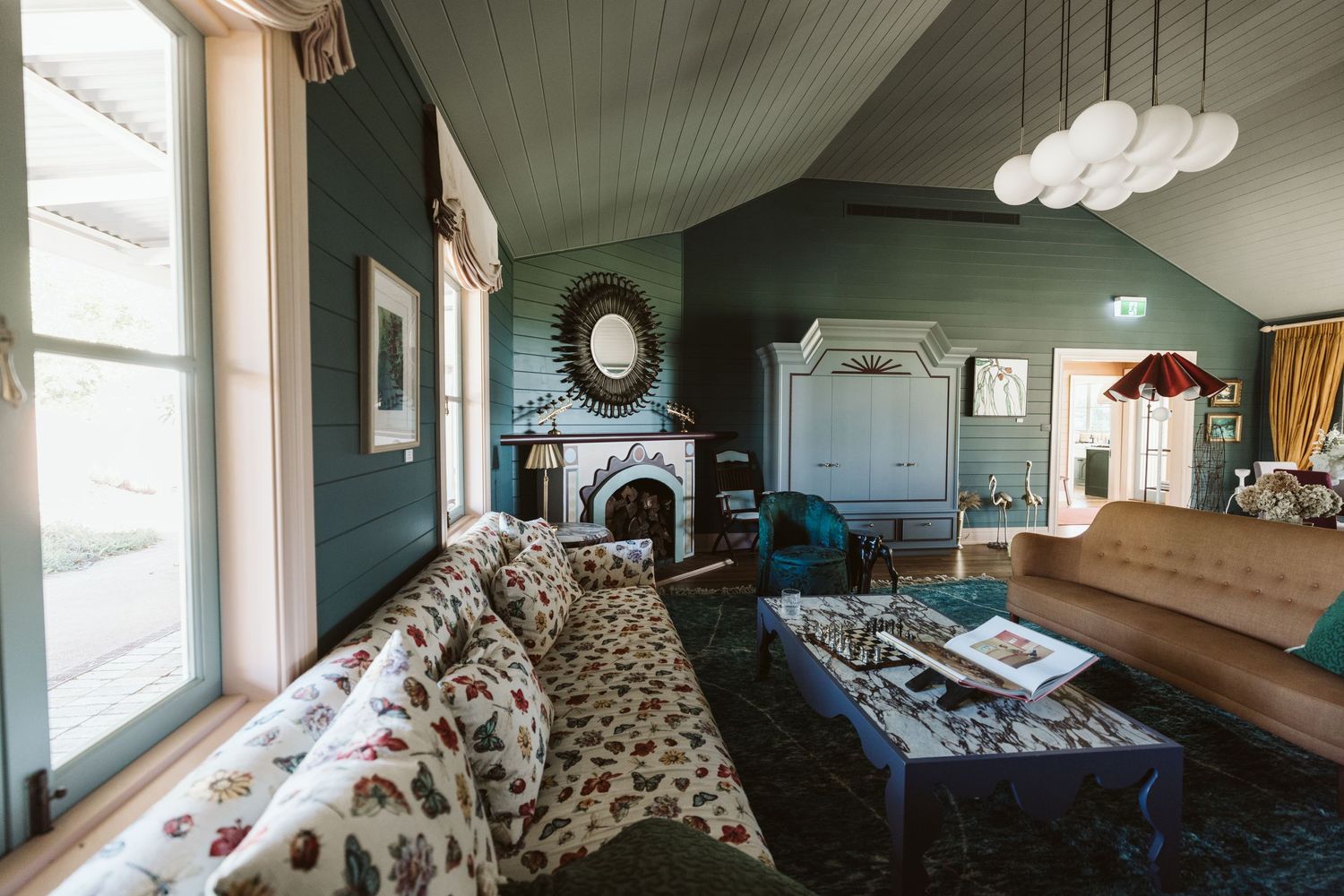 Elegant living room with dark teal walls, vintage fireplace, and plush spotted couch in a coastal cottage.