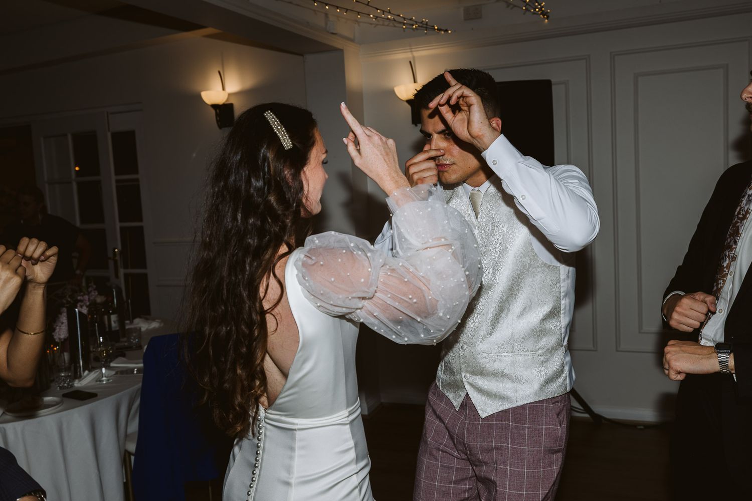 Bride and groom dancing energetically at wedding reception in elegant venue.