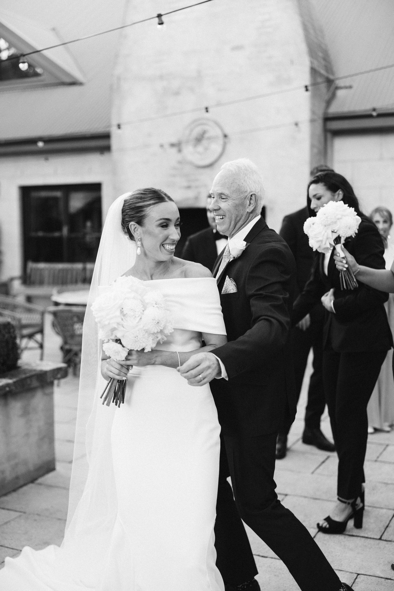 Black and white photo of bride sharing dance with older gentleman at outdoor wedding reception.