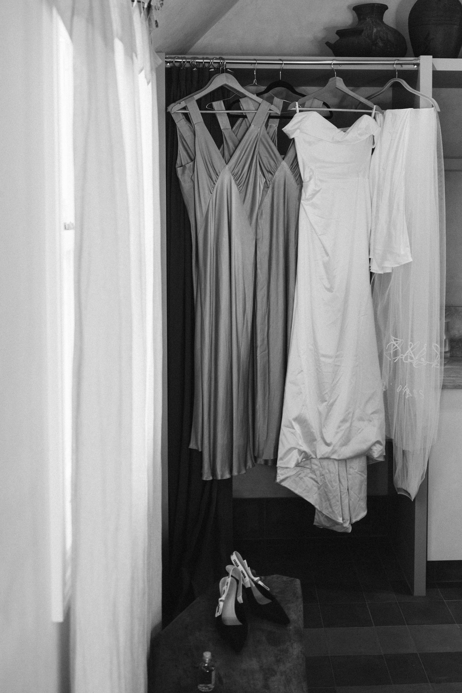 A white wedding dress and gray bridesmaid dresses hang in a closet with a pair of shoes below.
