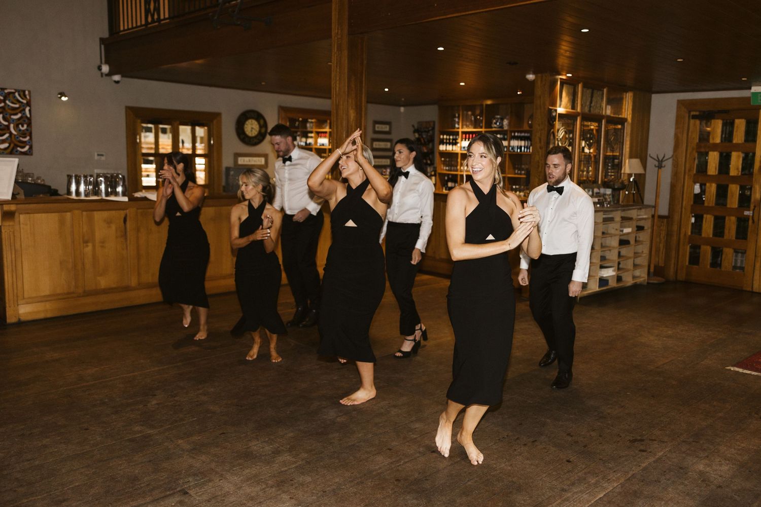 Wedding guests dancing in rustic indoor venue with wooden decor.