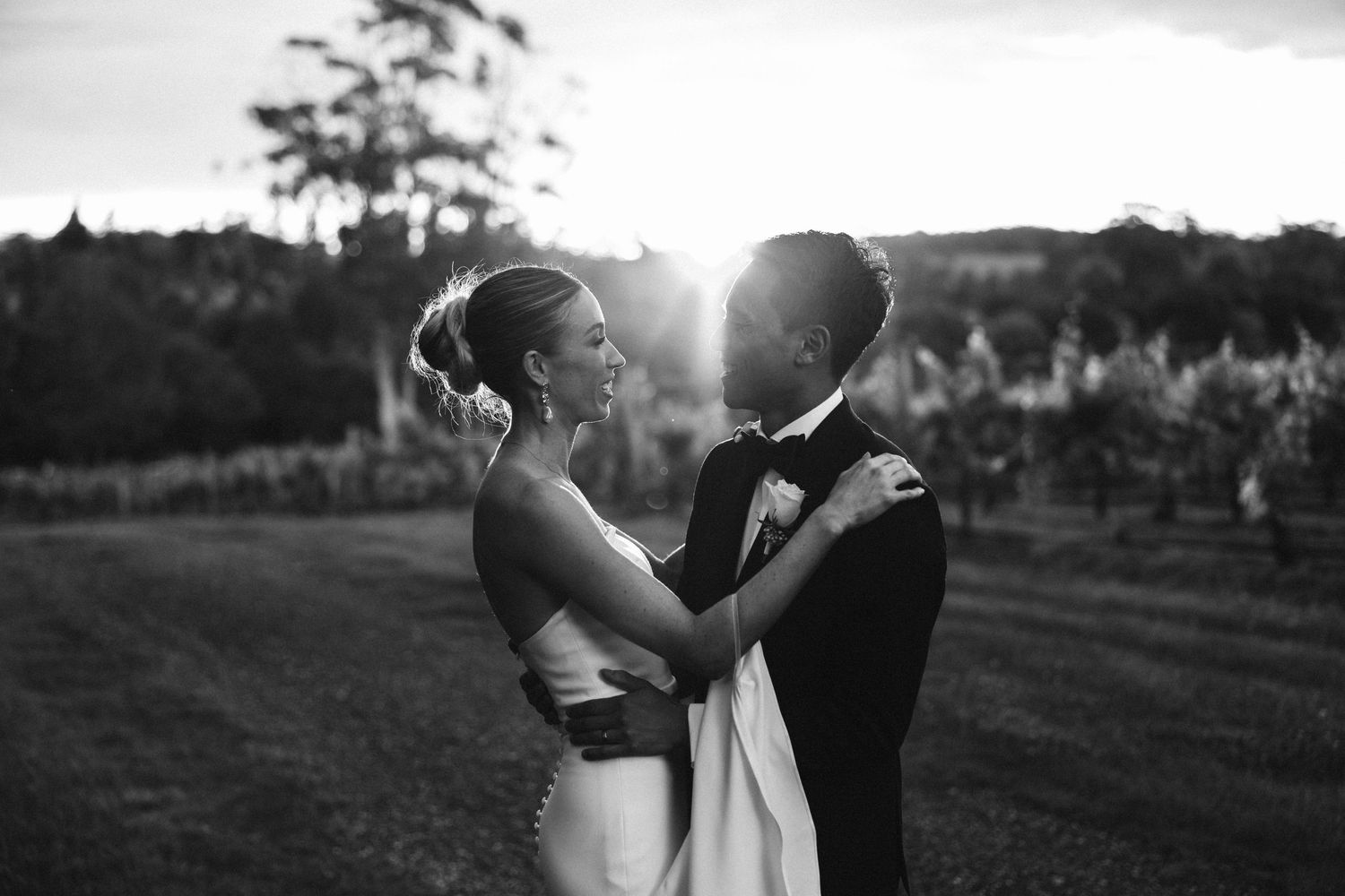 A romantic silhouette of newlyweds embracing in front of a sunset vineyard landscape.