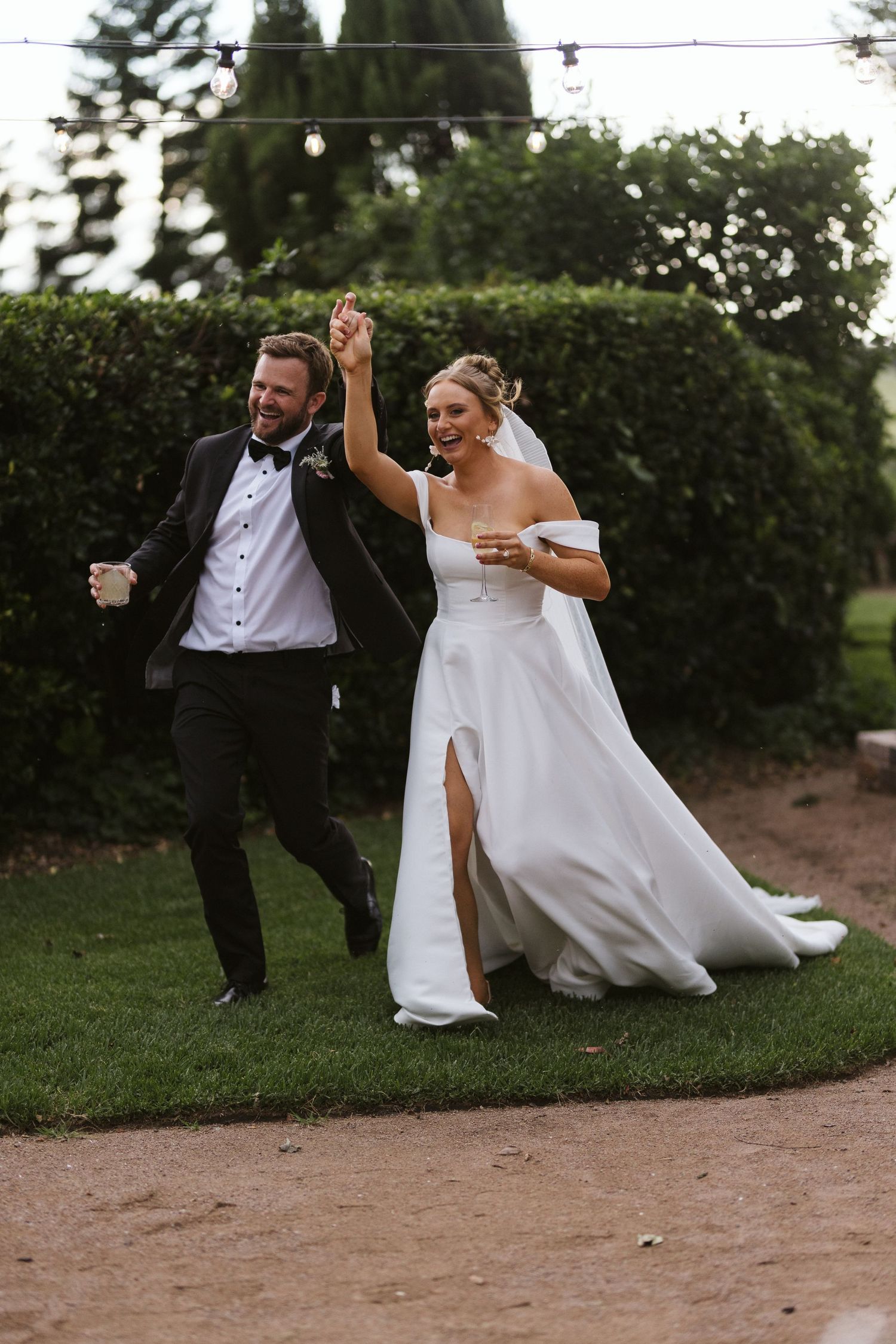 A celebratory moment as a couple in wedding attire dance together on a garden path surrounded by greenery.