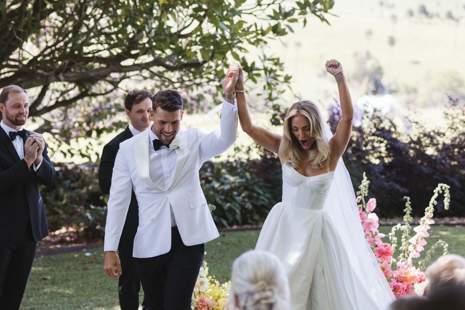 A joyful newlywed couple celebrates with raised arms during their outdoor garden wedding ceremony.