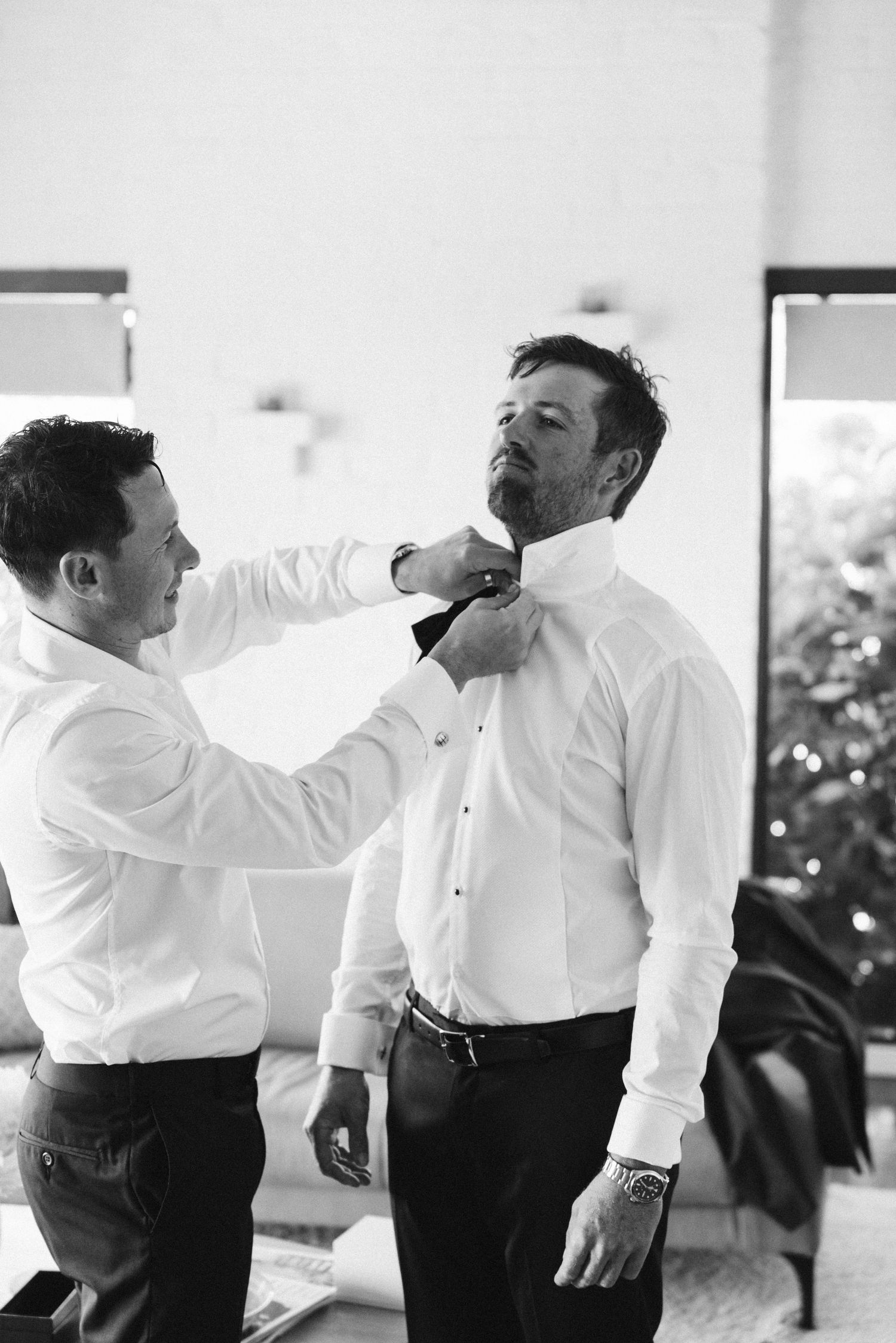 Two people in white shirts adjusting a bow tie during formal event preparation.