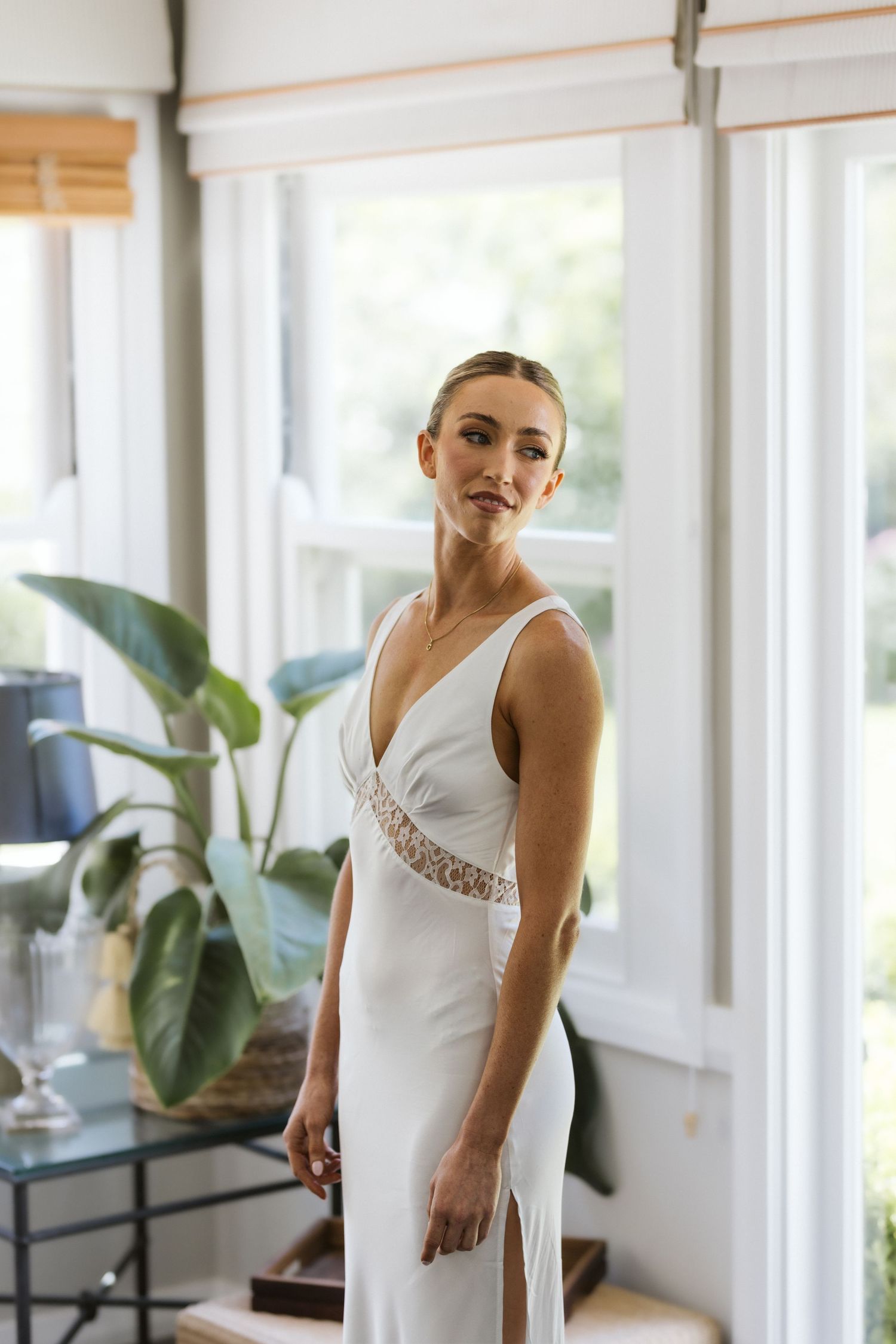 Elegant white wedding dress being modeled in a sun-filled room with natural decor.