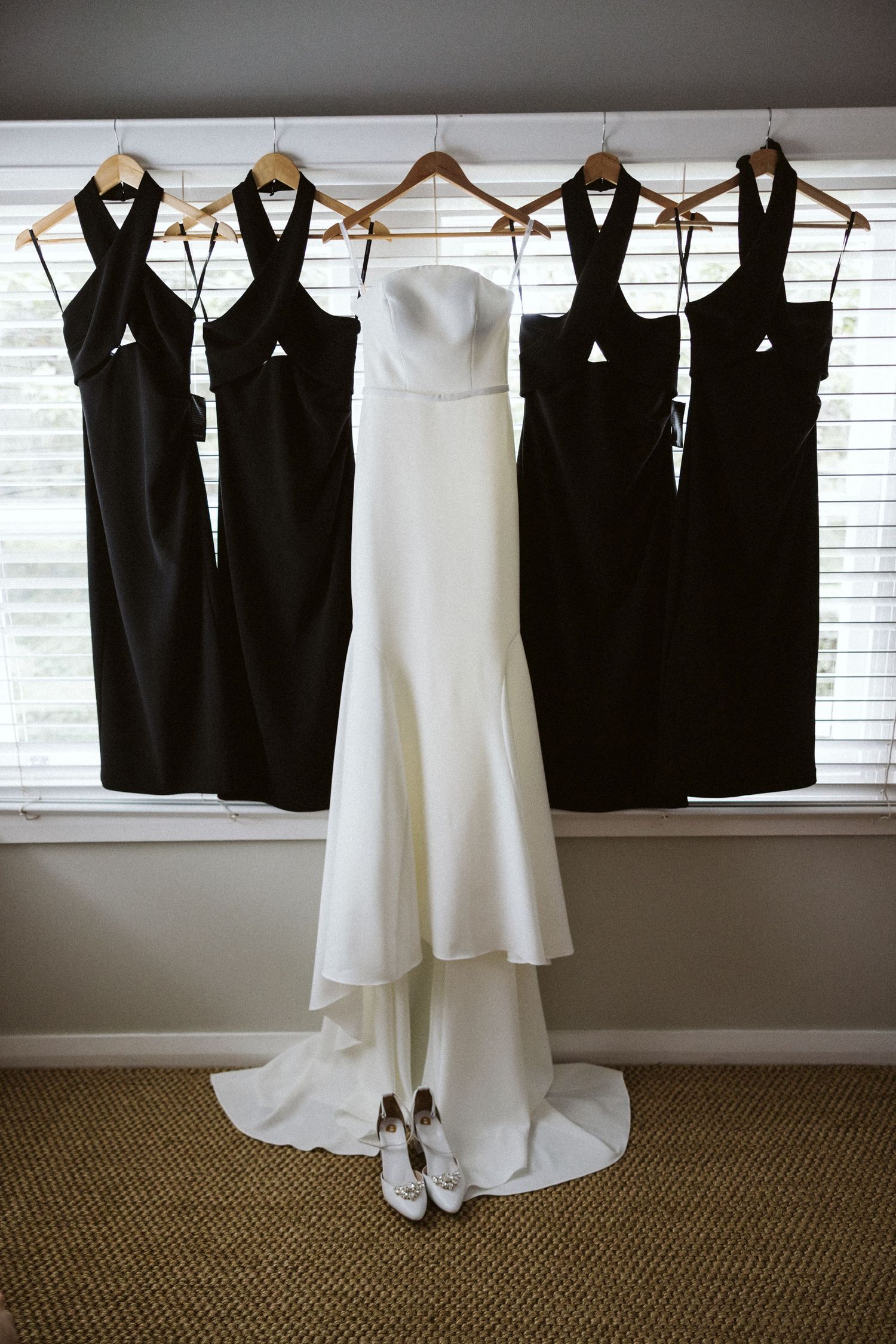 Wedding party attire displayed on hangers featuring four black bridesmaid dresses and one white bridal gown.