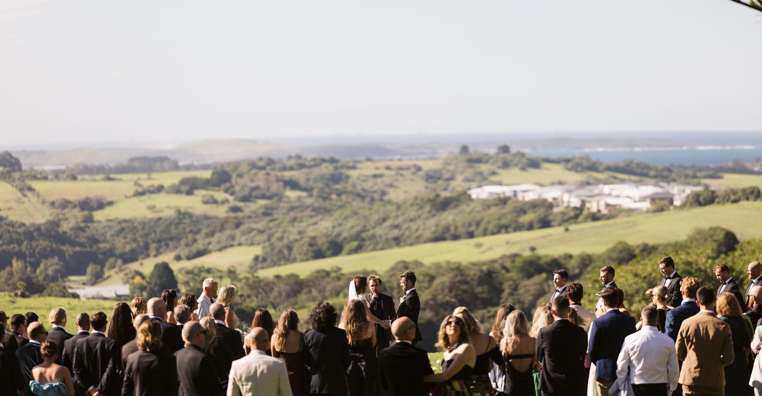 Large wedding gathering on a hilltop overlooking rolling countryside views.
