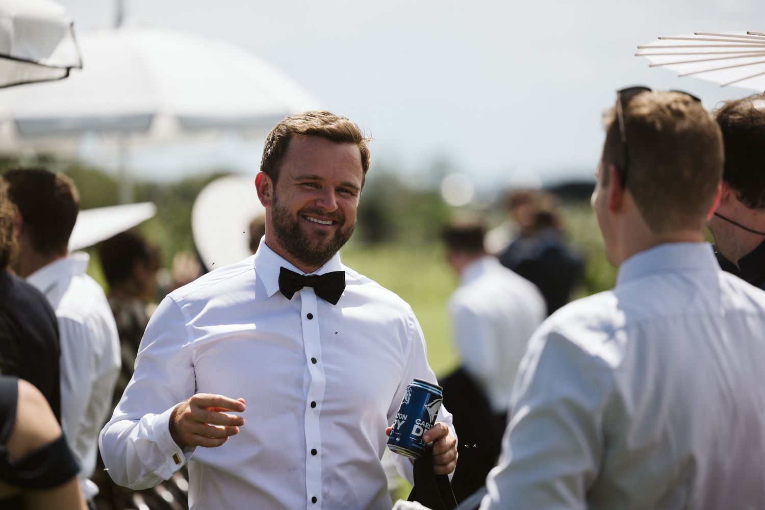 Smiling gentleman in bow tie and formal attire enjoying outdoor event.