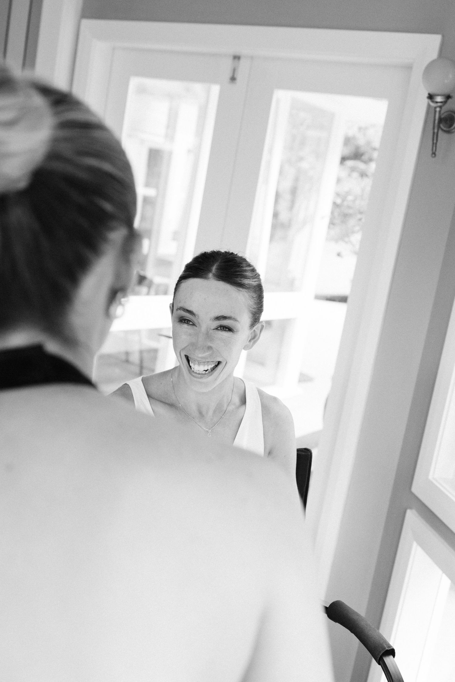 Candid black and white photograph capturing a moment of laughter during wedding preparations.