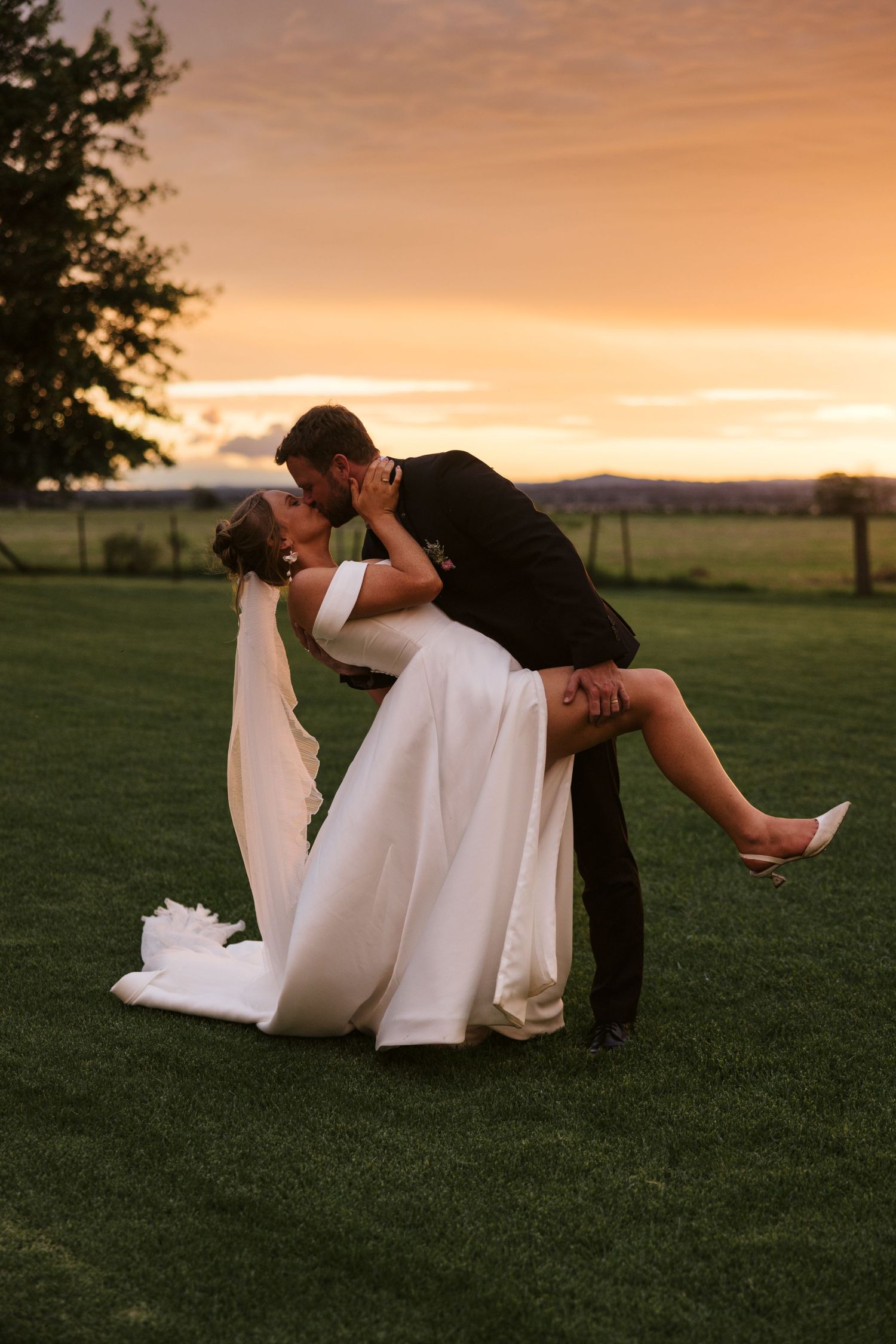 Romantic dip kiss pose during golden hour sunset on wedding day.