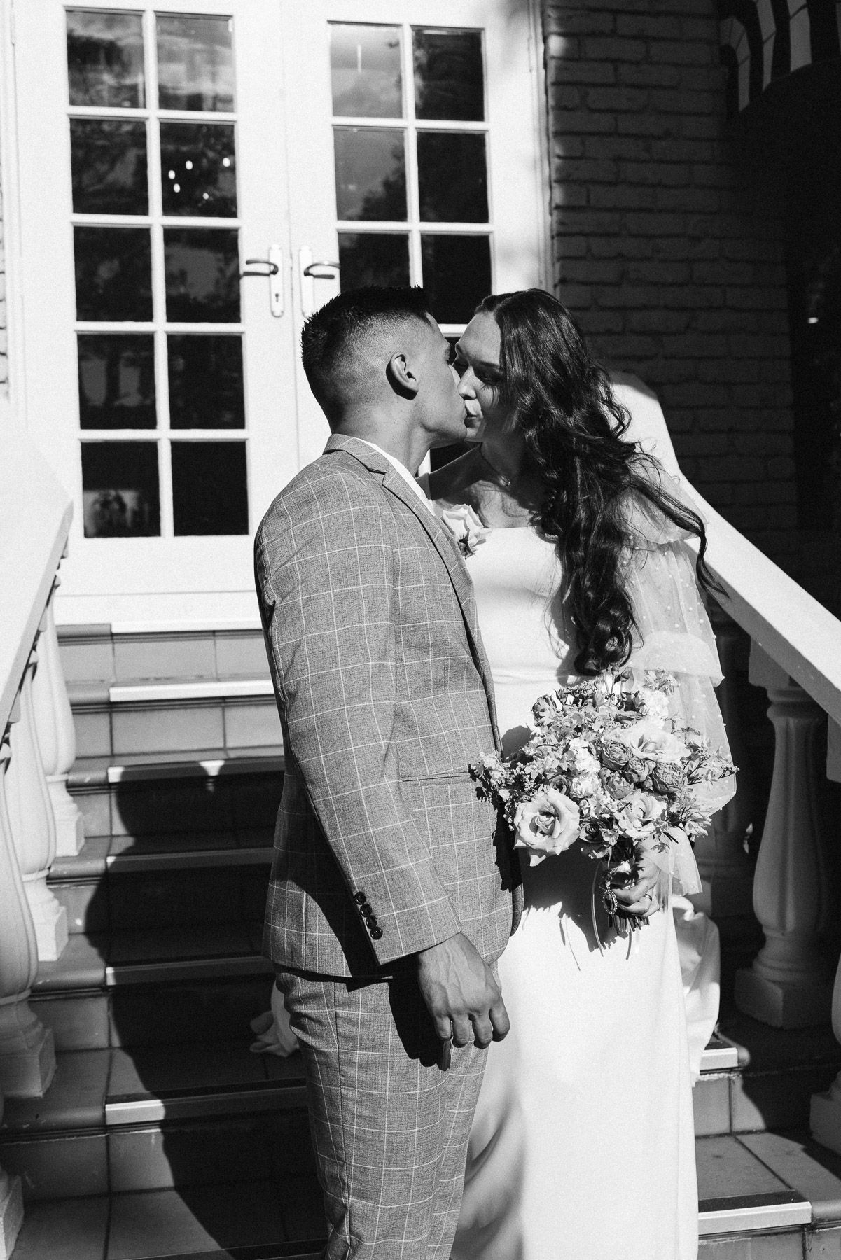 Black and white photo of a bride and groom sharing a tender moment on steps, bride holding a bouquet.