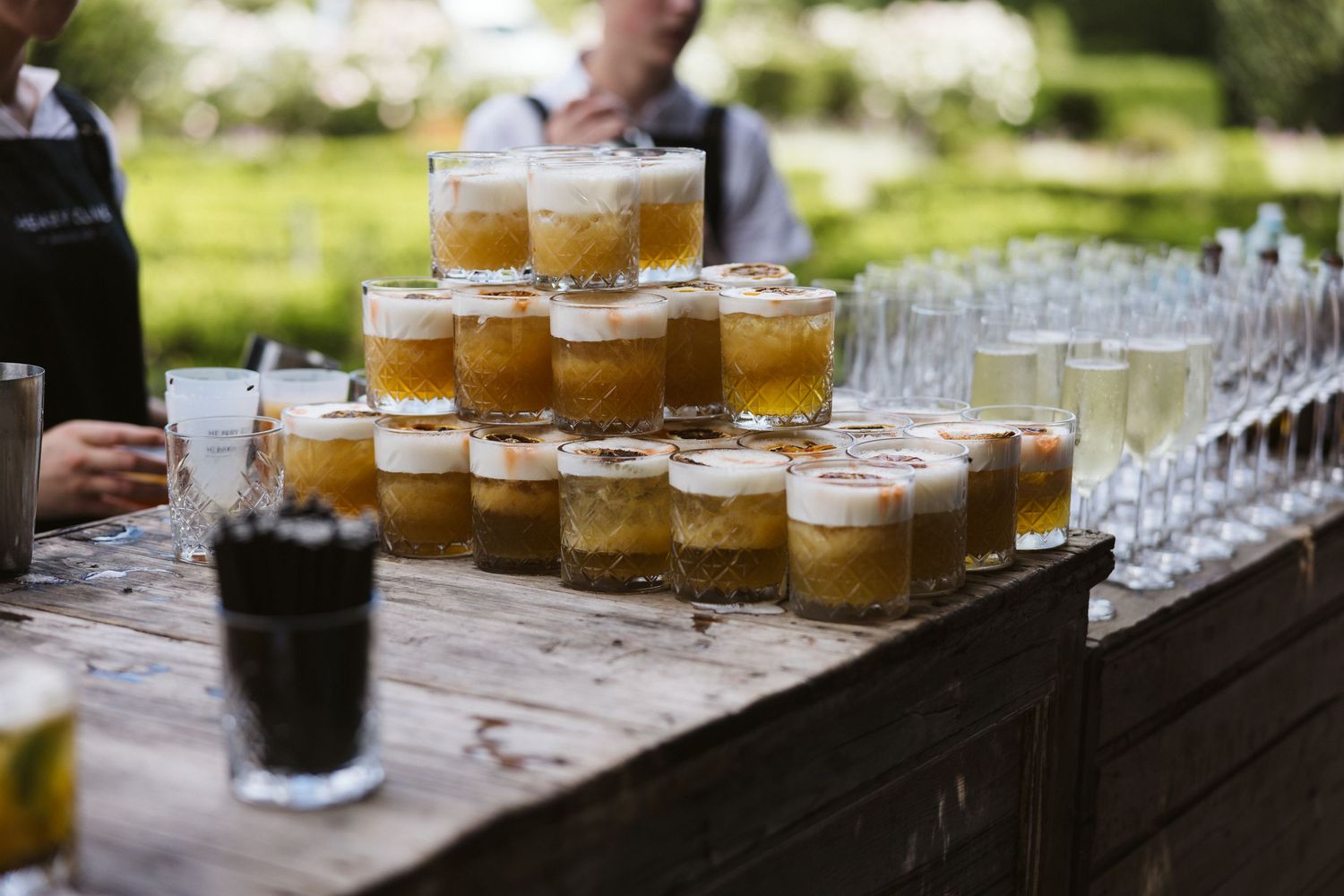Rustic wedding bar setup with rows of craft beer and cocktail glasses outdoors.