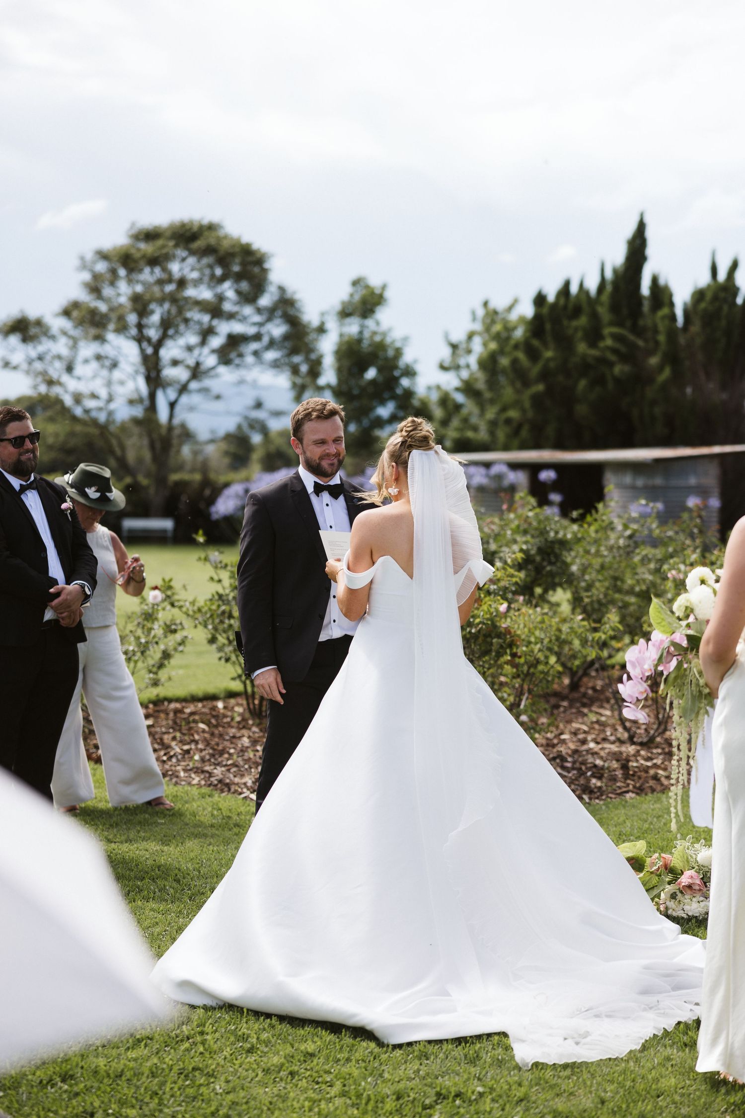 Wedding ceremony in progress with flowing white dress and garden landscape.