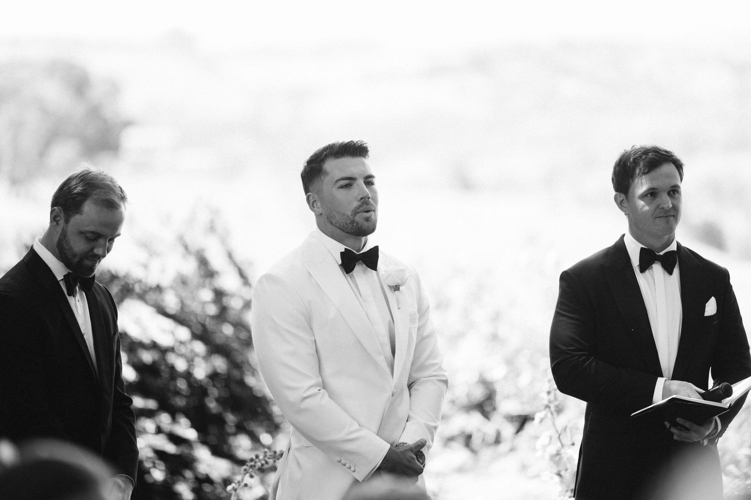 Black and white photo of groom and groomsmen during outdoor wedding ceremony.