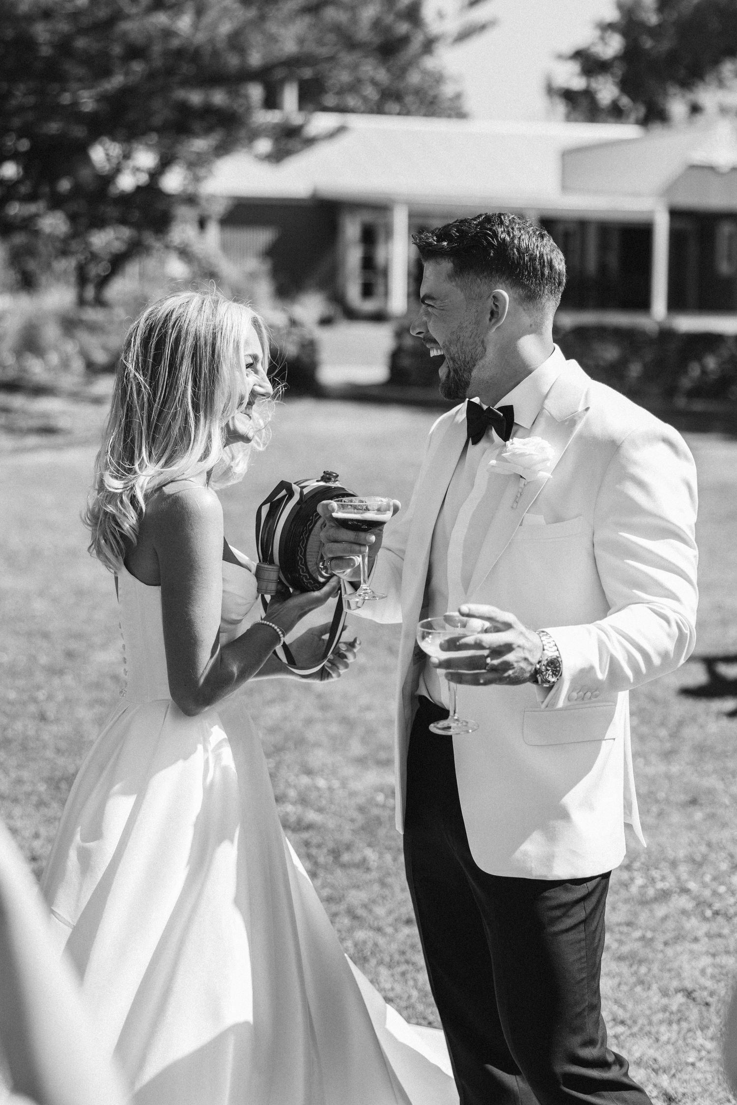 A black and white candid moment of two people laughing while holding drinks at an outdoor event.