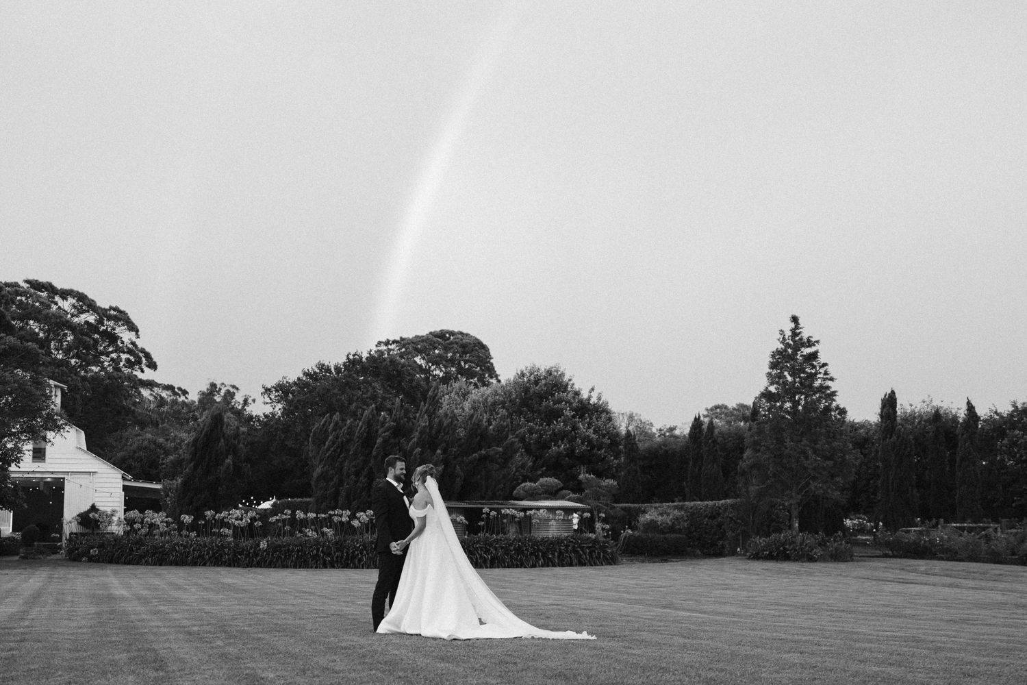 A dramatic black and white wedding portrait shows newlyweds standing on a vast lawn with a comet in the sky.