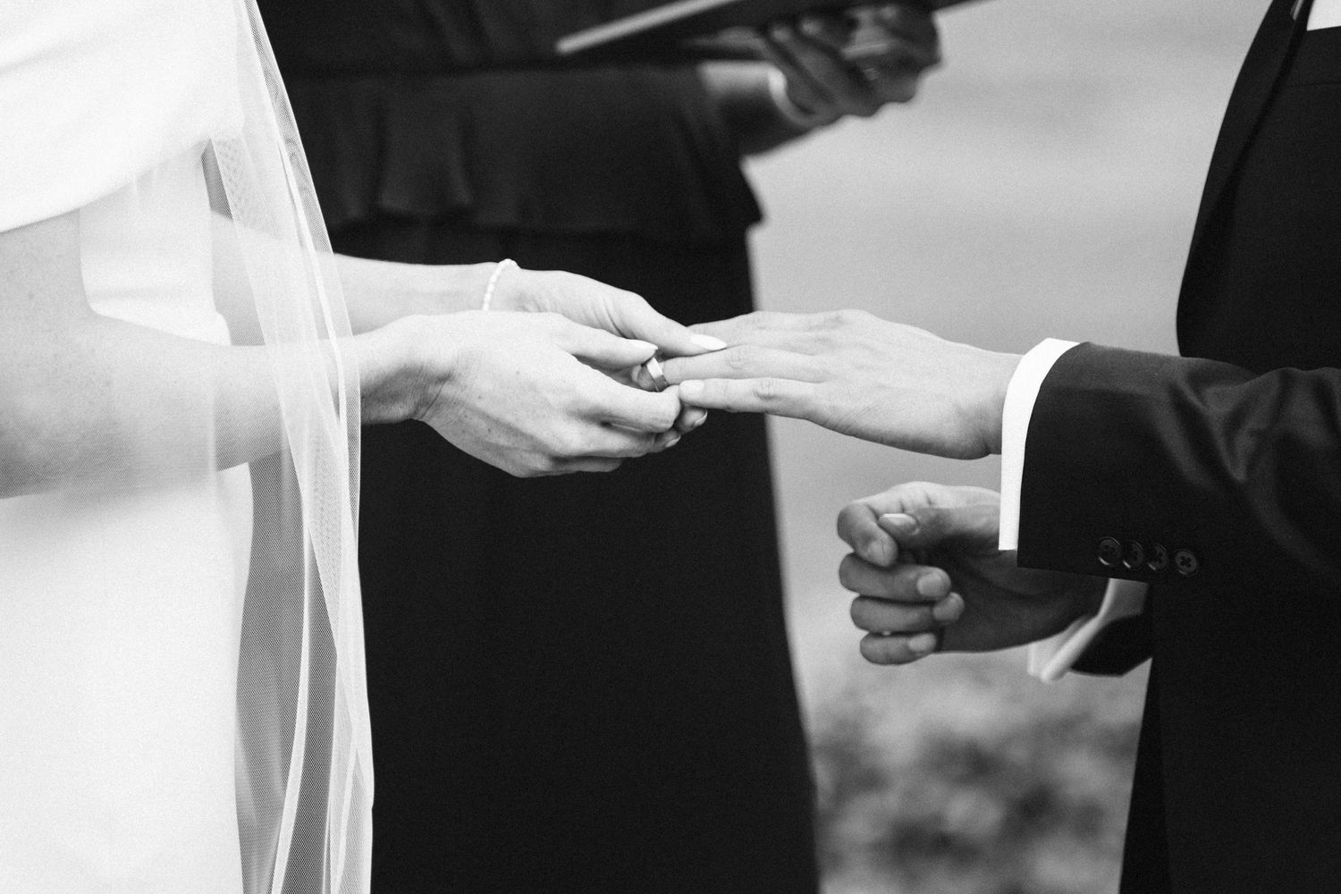 Black and white close-up of wedding ring exchange during ceremony.