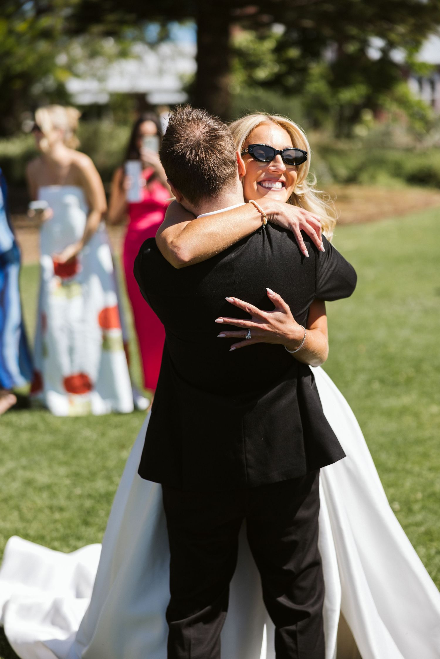 A loving embrace between two people at an outdoor wedding with guests in background.