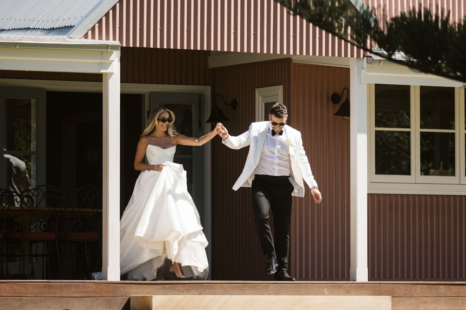 Newlyweds dance and celebrate on the porch of a rustic brown building.