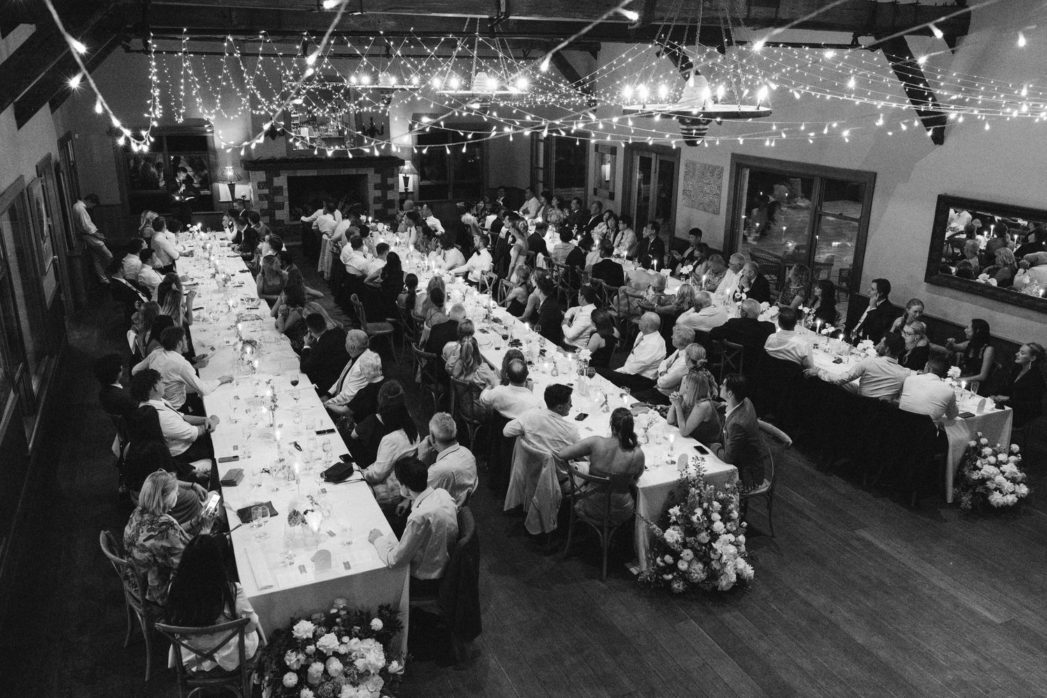 An aerial view of a wedding reception with long tables and string lights in black and white.
